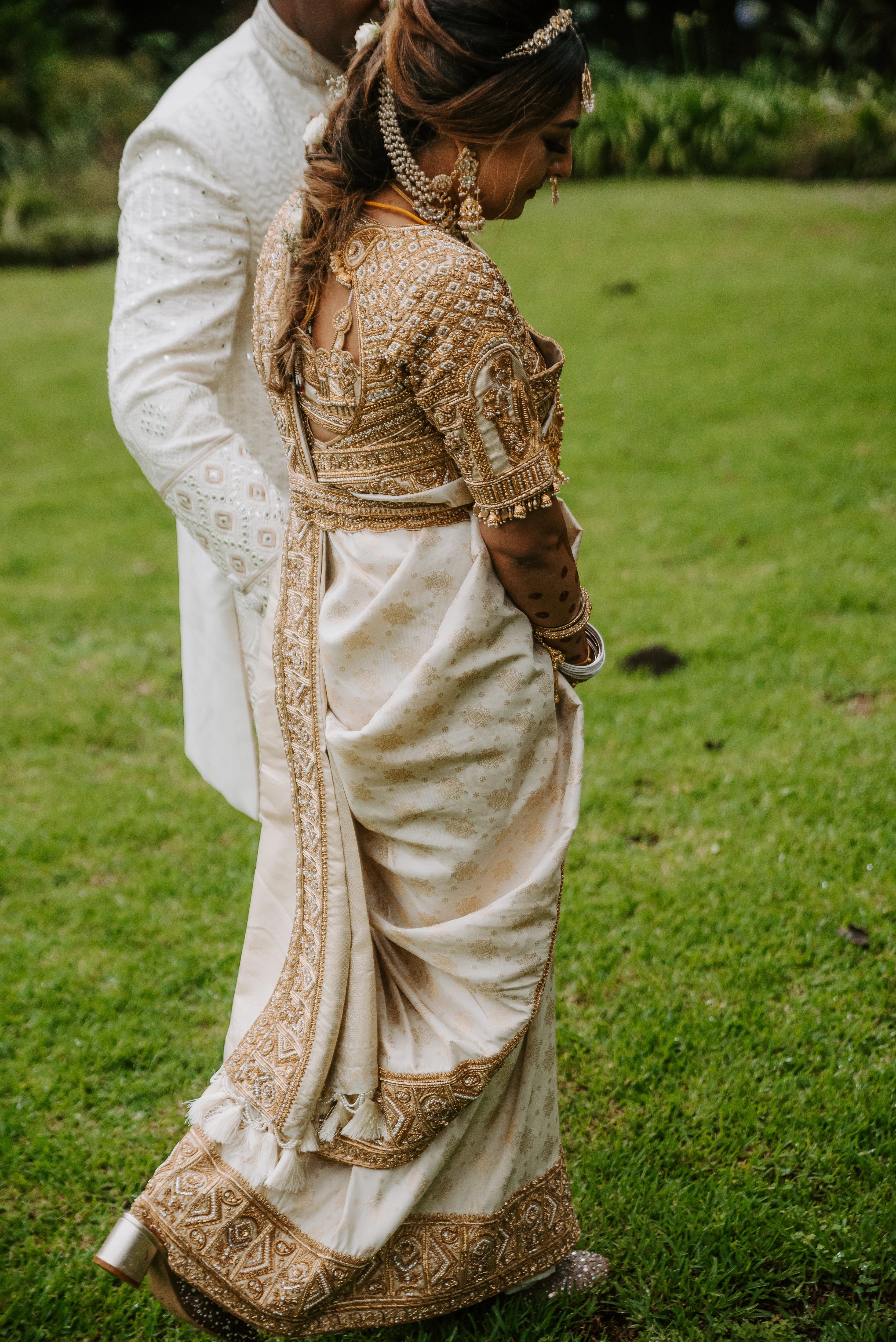 Bride Shayal Raniga walking with groom in an ivory silk concept blouse & saree border, intricately handcrafted with zardozi, stones, pearls and coins by team Archana Karthick.