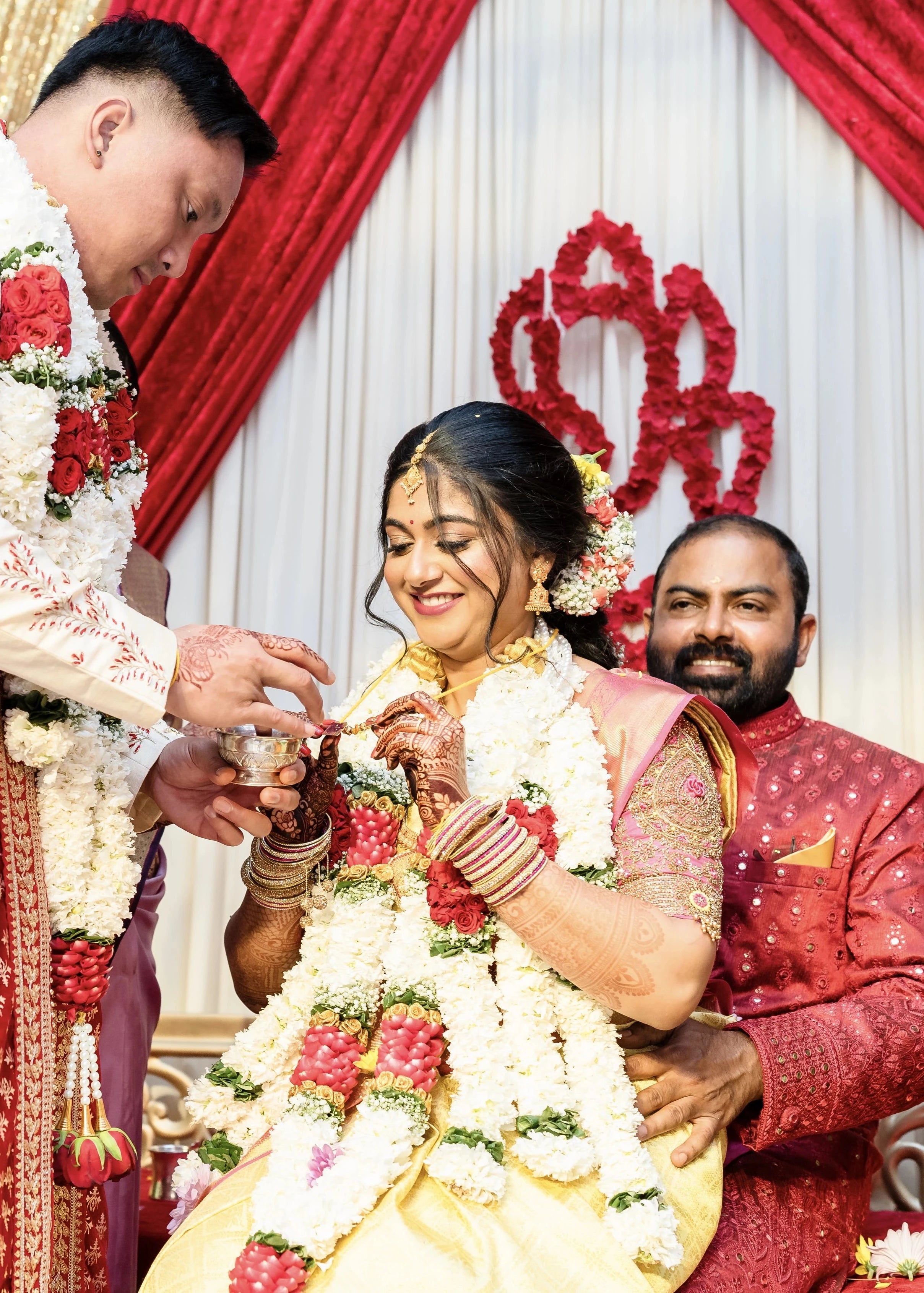Bride Shivani smiling during ritual in a pink silk blouse & belt, intricately handcrafted with beads, stones, resham, sequins and zardozi by team Archana Karthick.