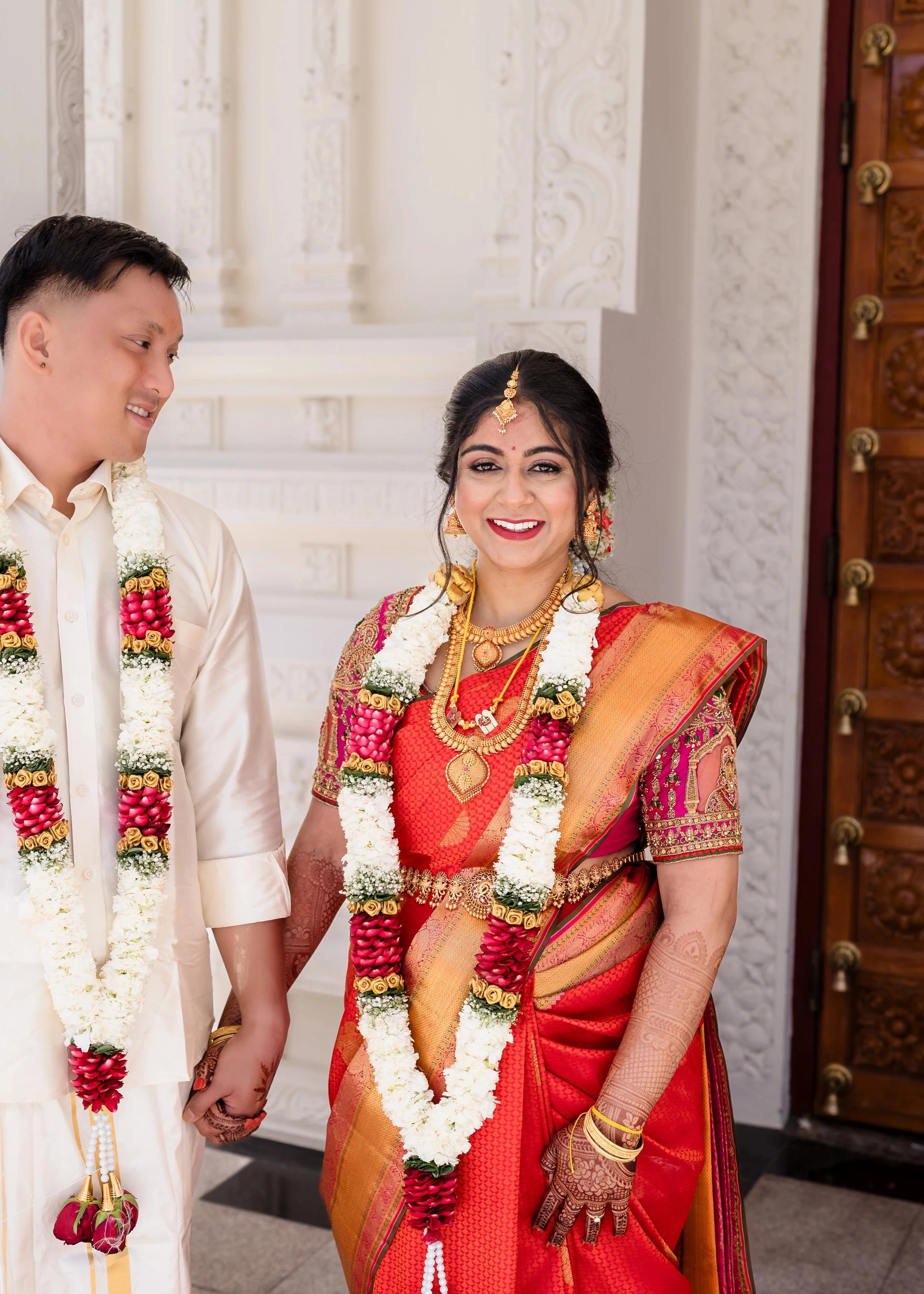 Bride Shivani smiling with groom in a magenta silk blouse, intricately handcrafted with beads, stones, resham, mirrors, jhumkas and zardozi by team Archana Karthick.
