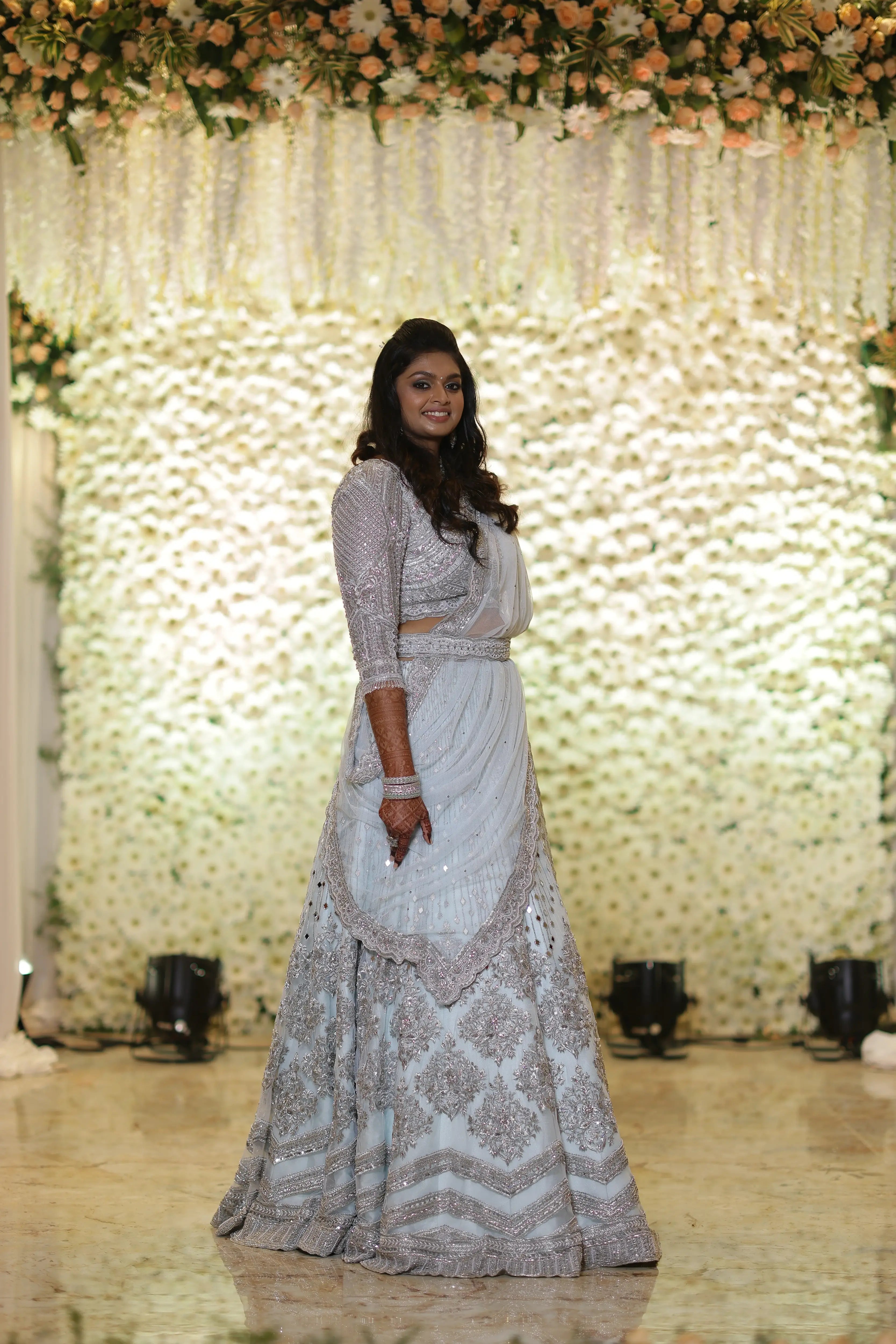 Bride Shreya from USA posing on stage for a side profile in a handcrafted powder blue net lehenga embellished with mirrors, pearls, zardozi, and crystals.