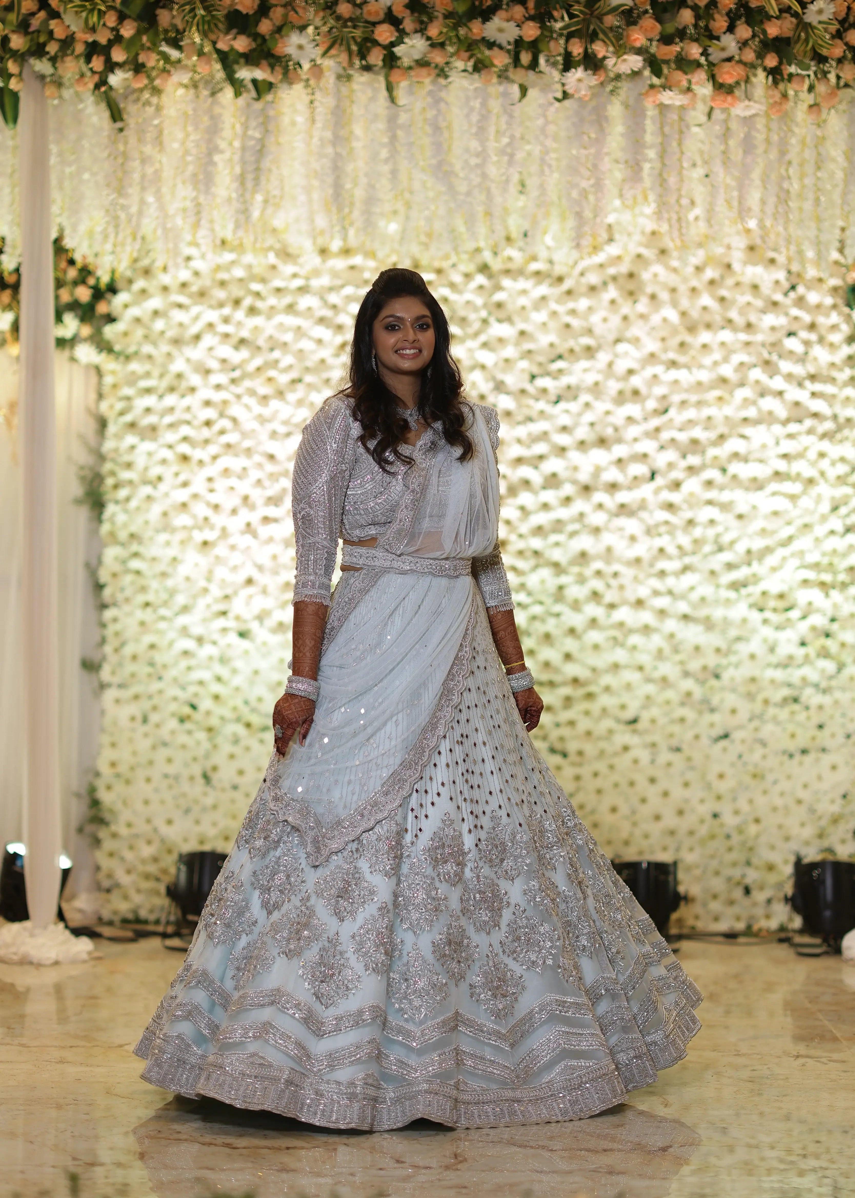 Bride Shreya from USA posing on stage showcasing the flare in a handcrafted powder blue net lehenga embellished with mirrors, pearls, zardozi, and crystals.