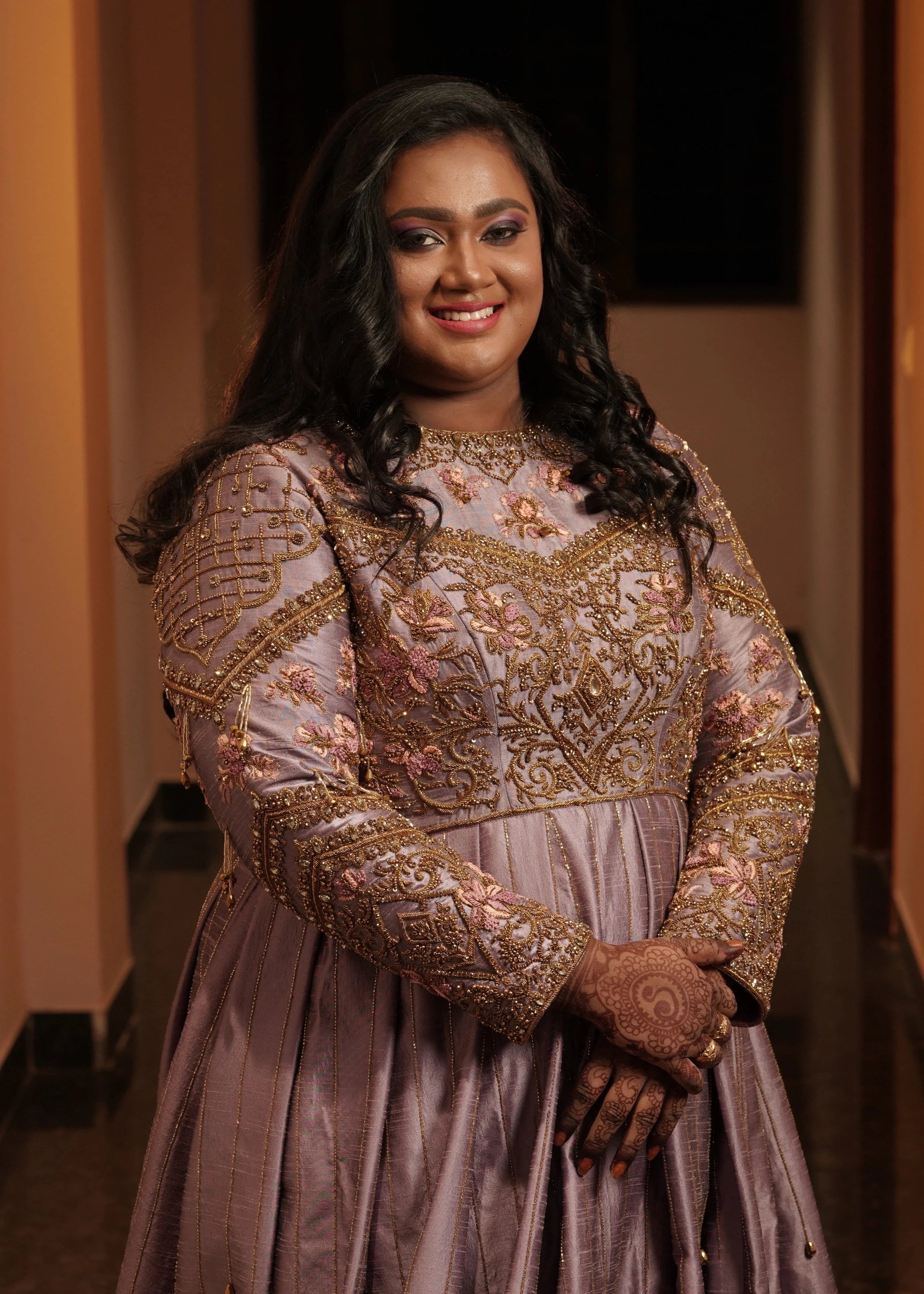 Bride Shyamaladevi smiling in a dusty mauve raw silk gown, intricately handcrafted with beads, cutdana, stones, resham and zardozi by team Archana Karthick.