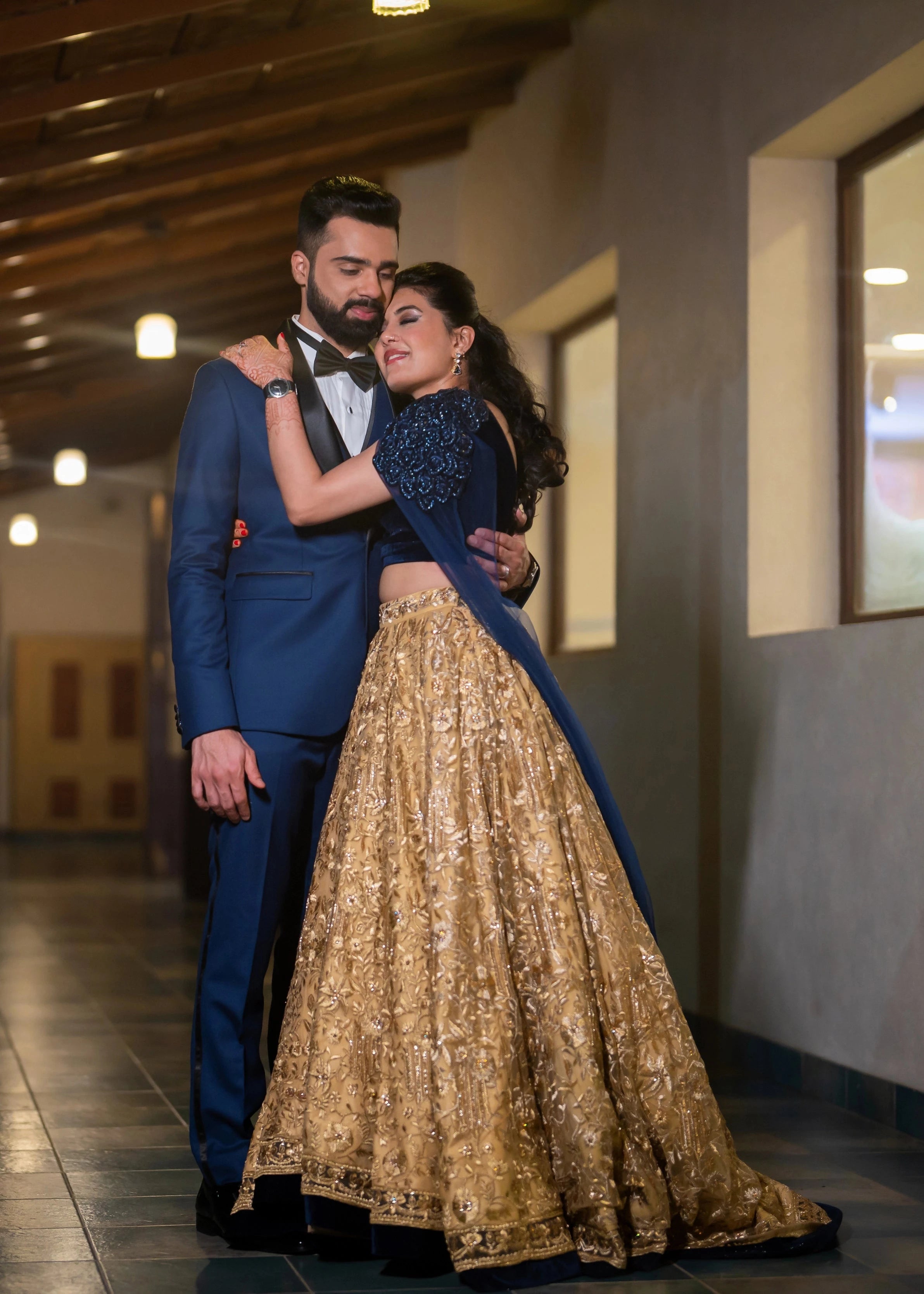 Bride Sneha Murugan posing with groom in a midnight blue (velvet) and gold (tulle) lehenga, intricately handcrafted with zari, sequins, cutdana and stones by team Archana Karthick.