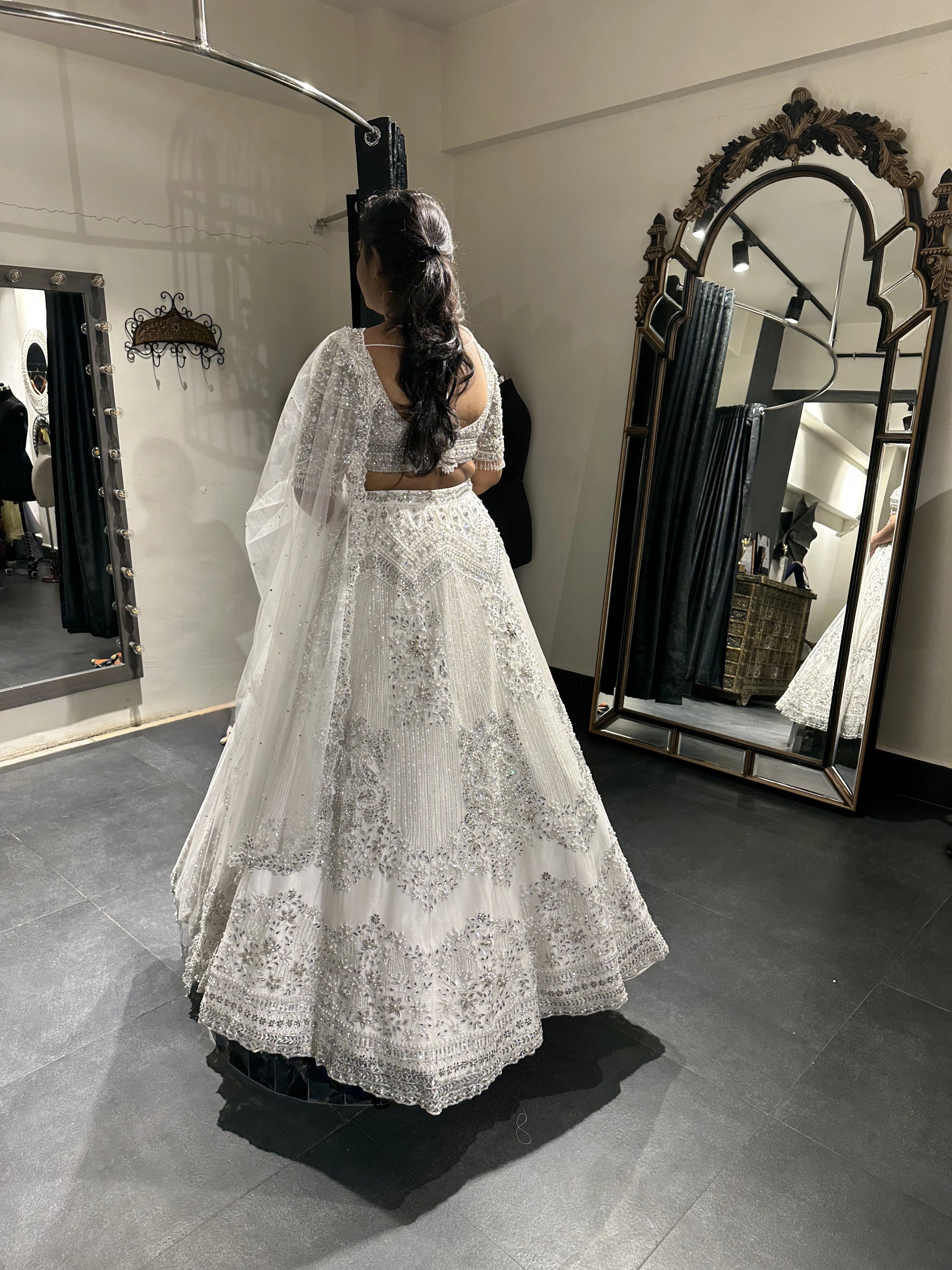 Bride Sneha from Chennai posing in front of a mirror in a silver raw silk lehenga, intricately handcrafted with zari, cutdana, zardozi, crystals and stones by team Archana Karthick.