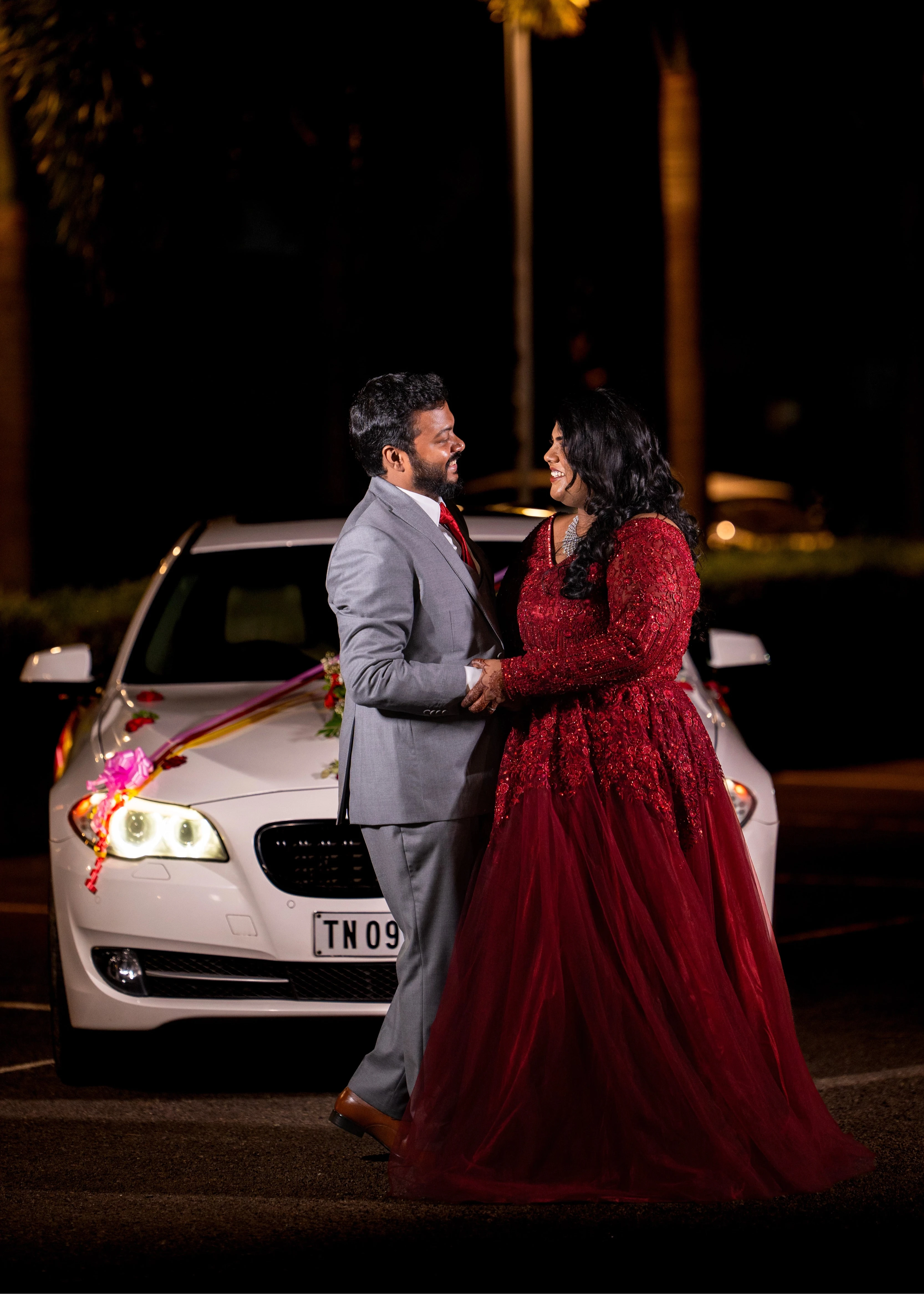 Bride Sushma in an embrace with groom in a red tulle gown, handcrafted intricately with resham, sequins, beads and cutdana by team Archana Karthick.
