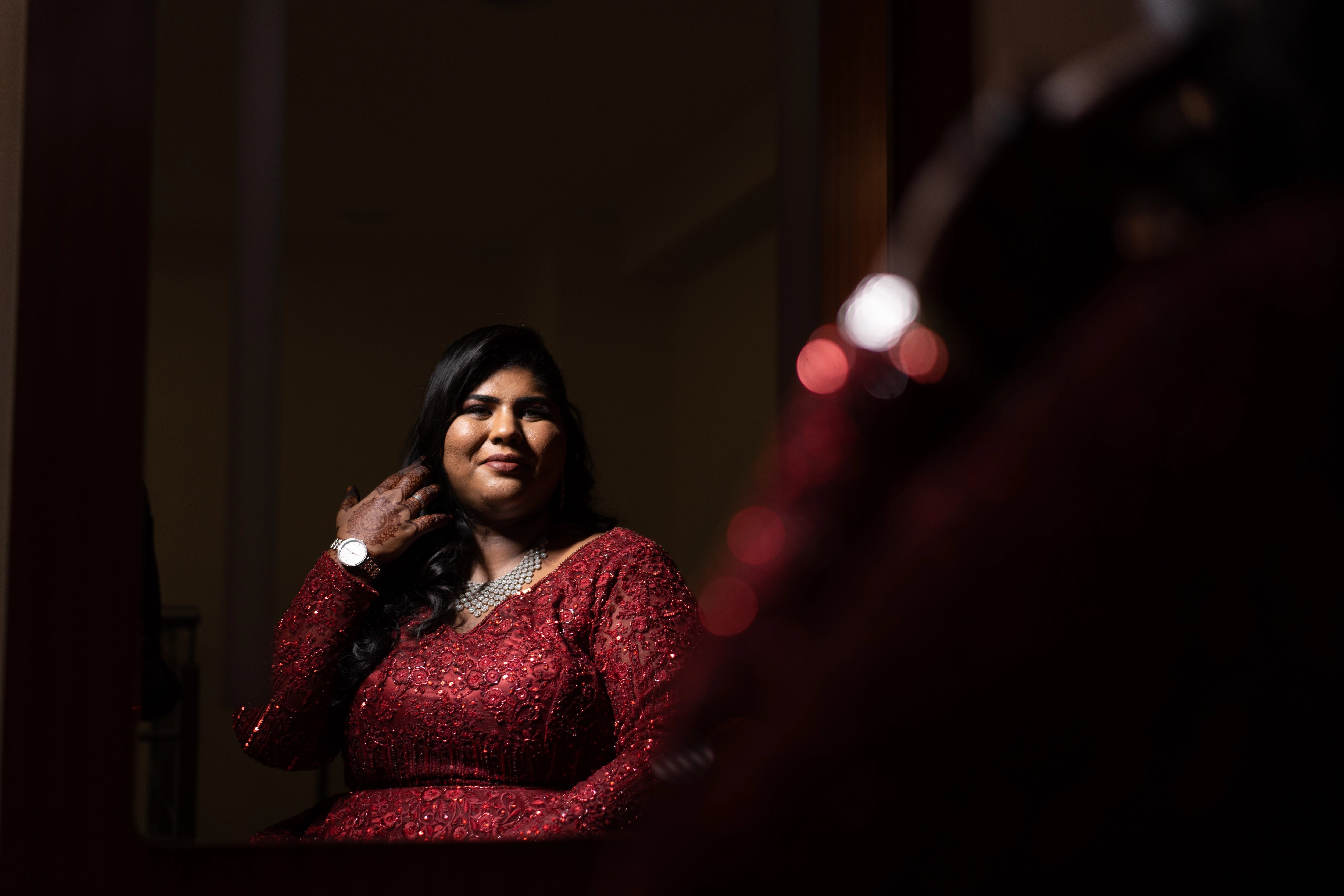 Bride Sushma looking at mirror in a red tulle gown, handcrafted intricately with resham, sequins, beads and cutdana by team Archana Karthick.