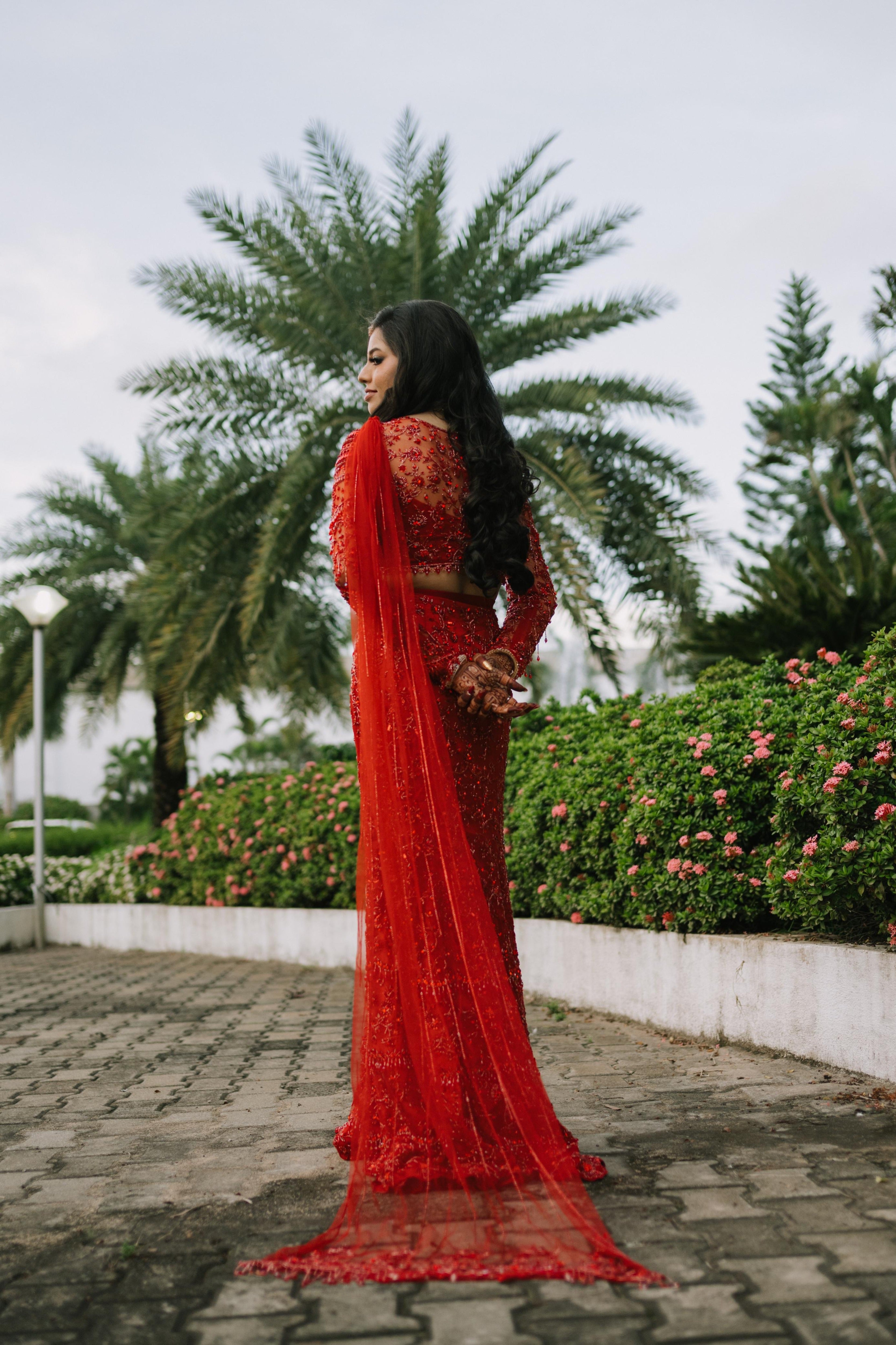 Bride Urmila posing elegantly for her reception in a red handcrafted mermaid lehenga drape designed by Archana Karthick. Back blouse and lehenga trail design captured.