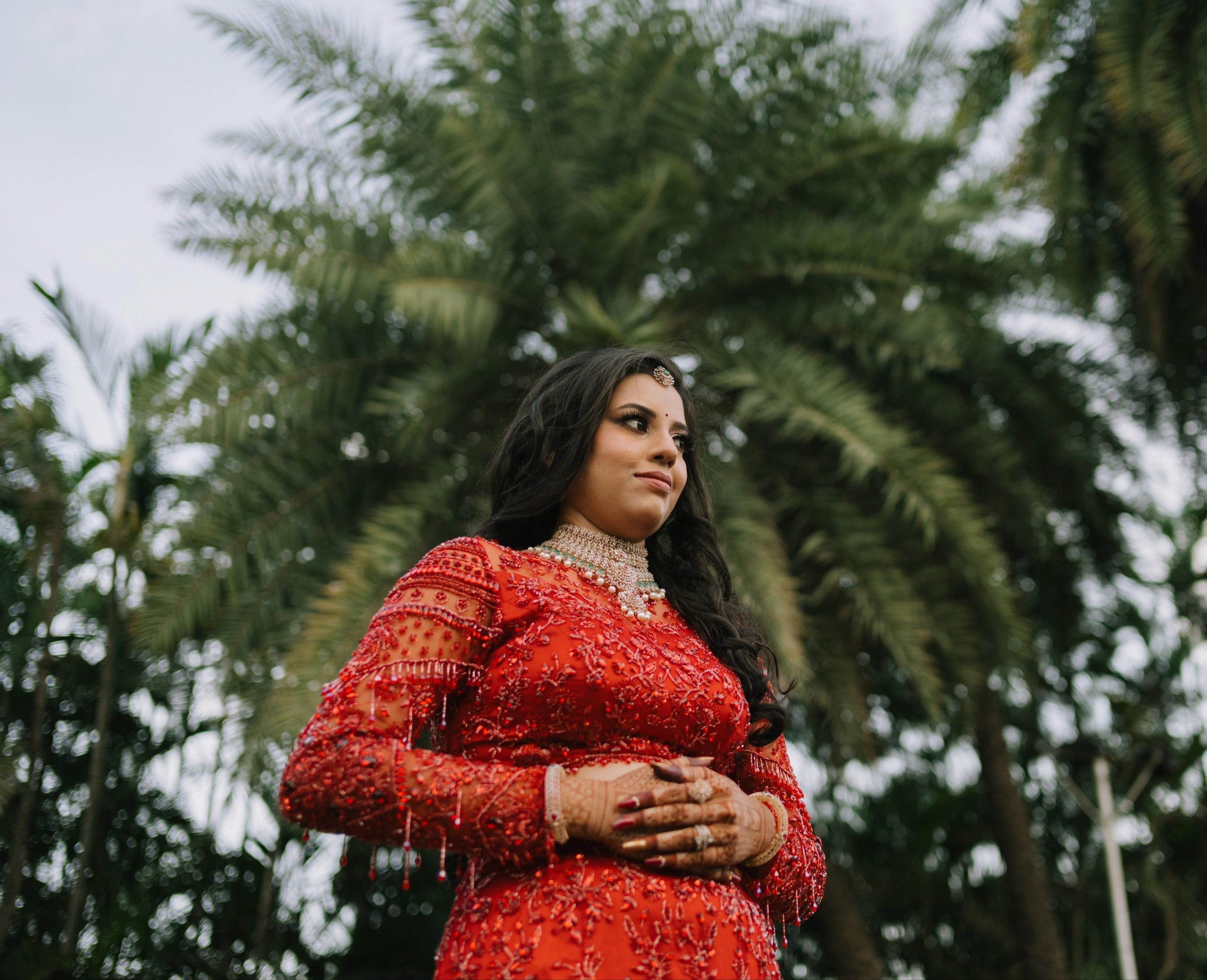 Bride Urmila posing elegantly for her reception in a red handcrafted mermaid lehenga drape designed by Archana Karthick. Full blouse front and sleeve hangings captured.