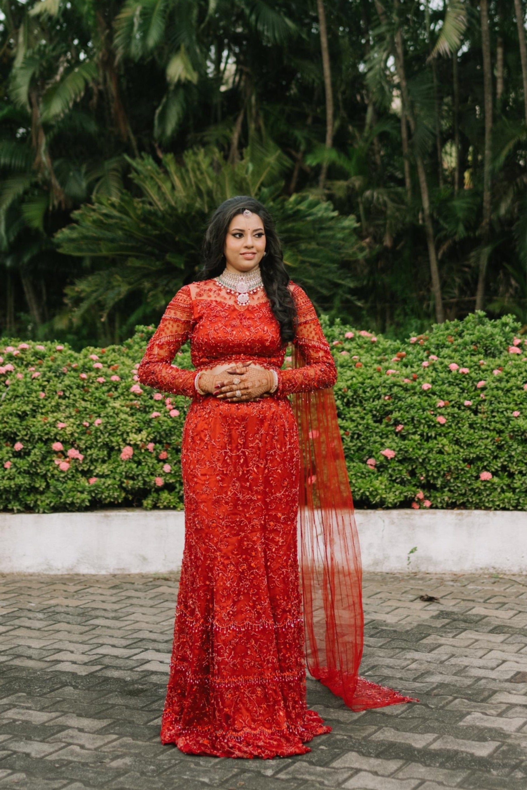 Bride Urmila posing elegantly for her reception in a red handcrafted mermaid lehenga drape designed by Archana Karthick. Full front profile.