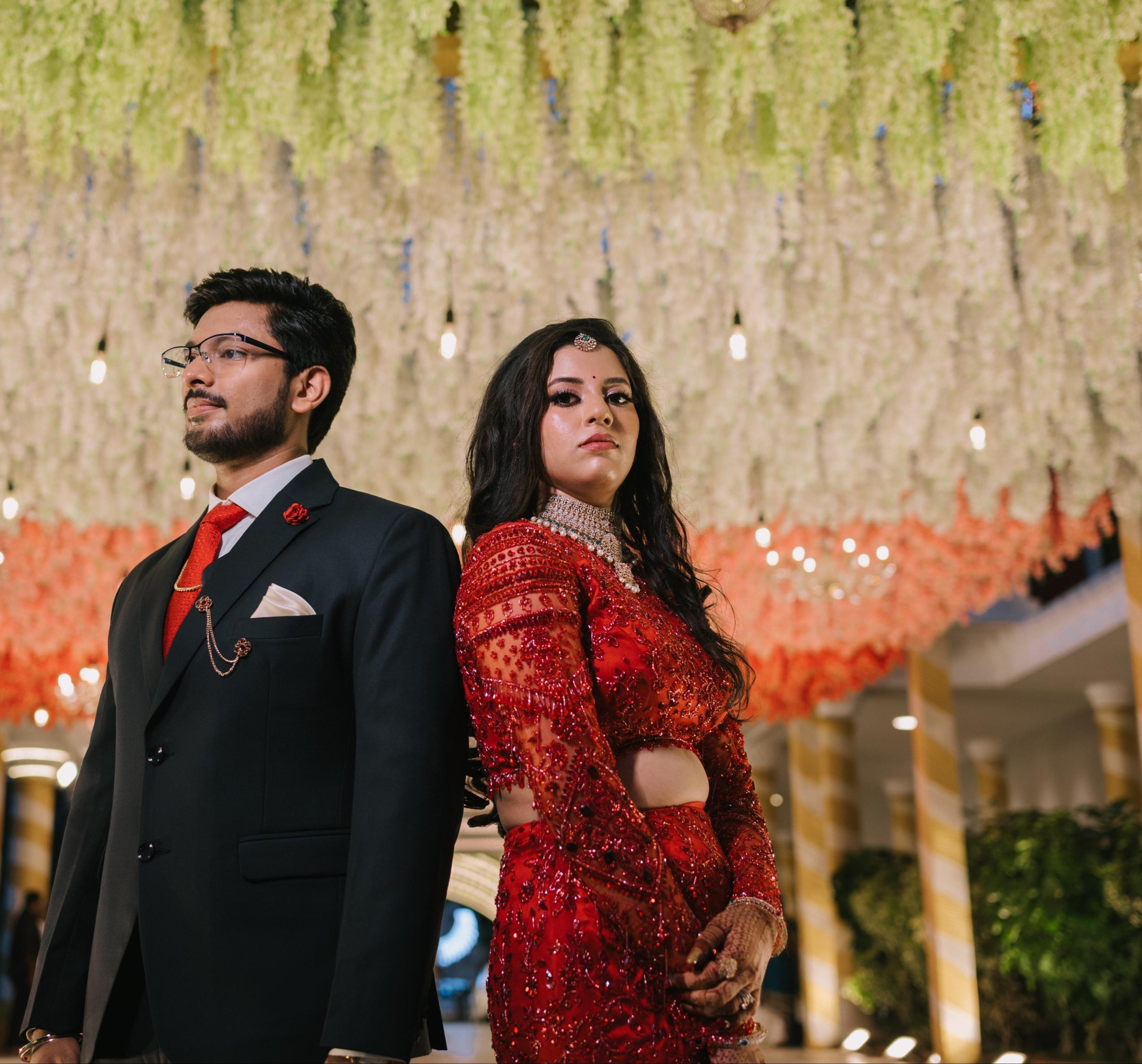 Bride Urmila posing elegantly with groom for her reception in a red handcrafted mermaid lehenga drape designed by Archana Karthick.