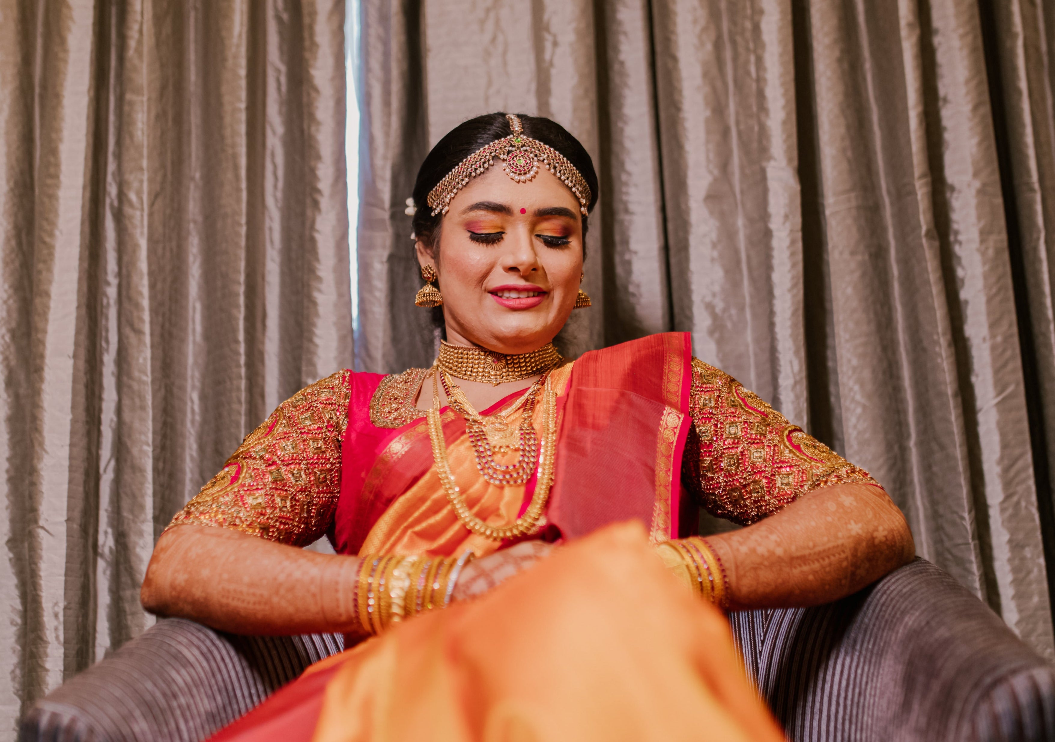 Bride Varshini in a handcrafted red silk blouse designed by Archana Karthick. Seated position facing the lens.
