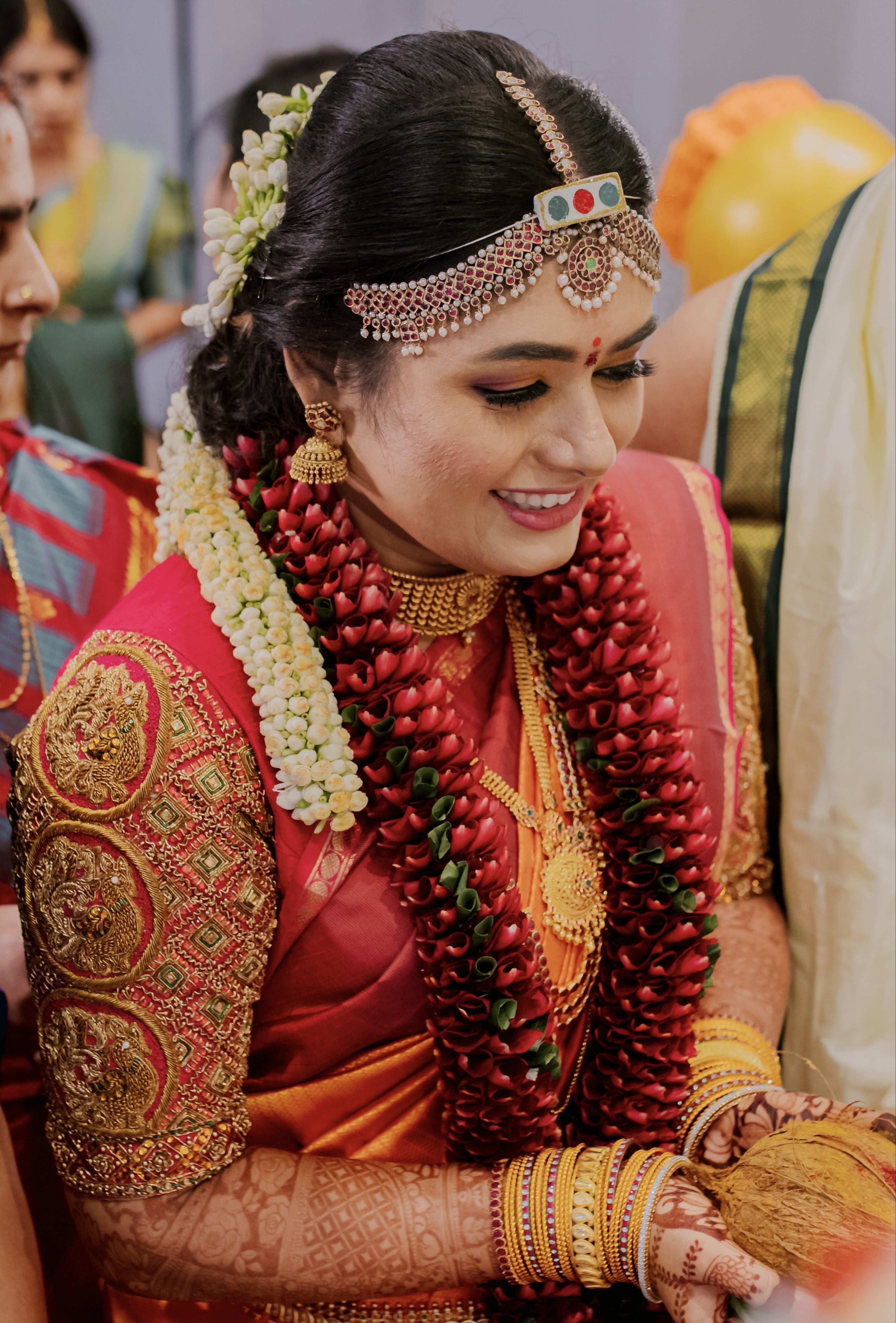 Bride Varshini in a handcrafted red silk blouse designed by Archana Karthick. She is in the middle of accepting the offerings and looking down.