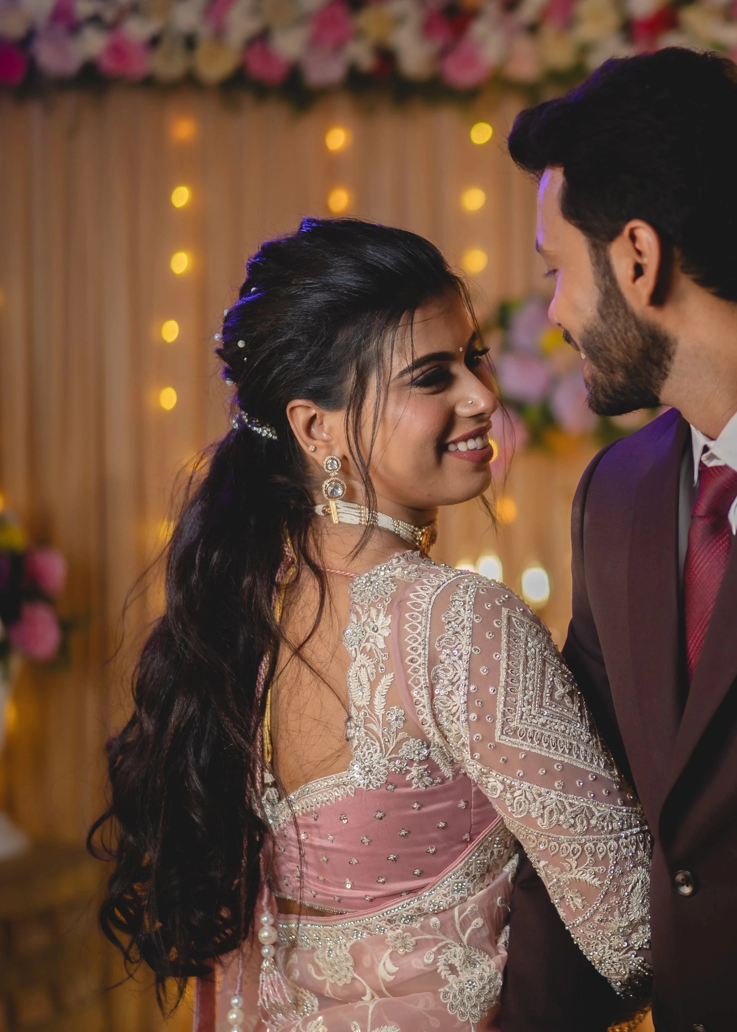 Bride Vidhira smiling with groom in a soft blush tulle blouse for her reception, handcrafted with rhinestones, resham and crystals by team Archana Karthick.