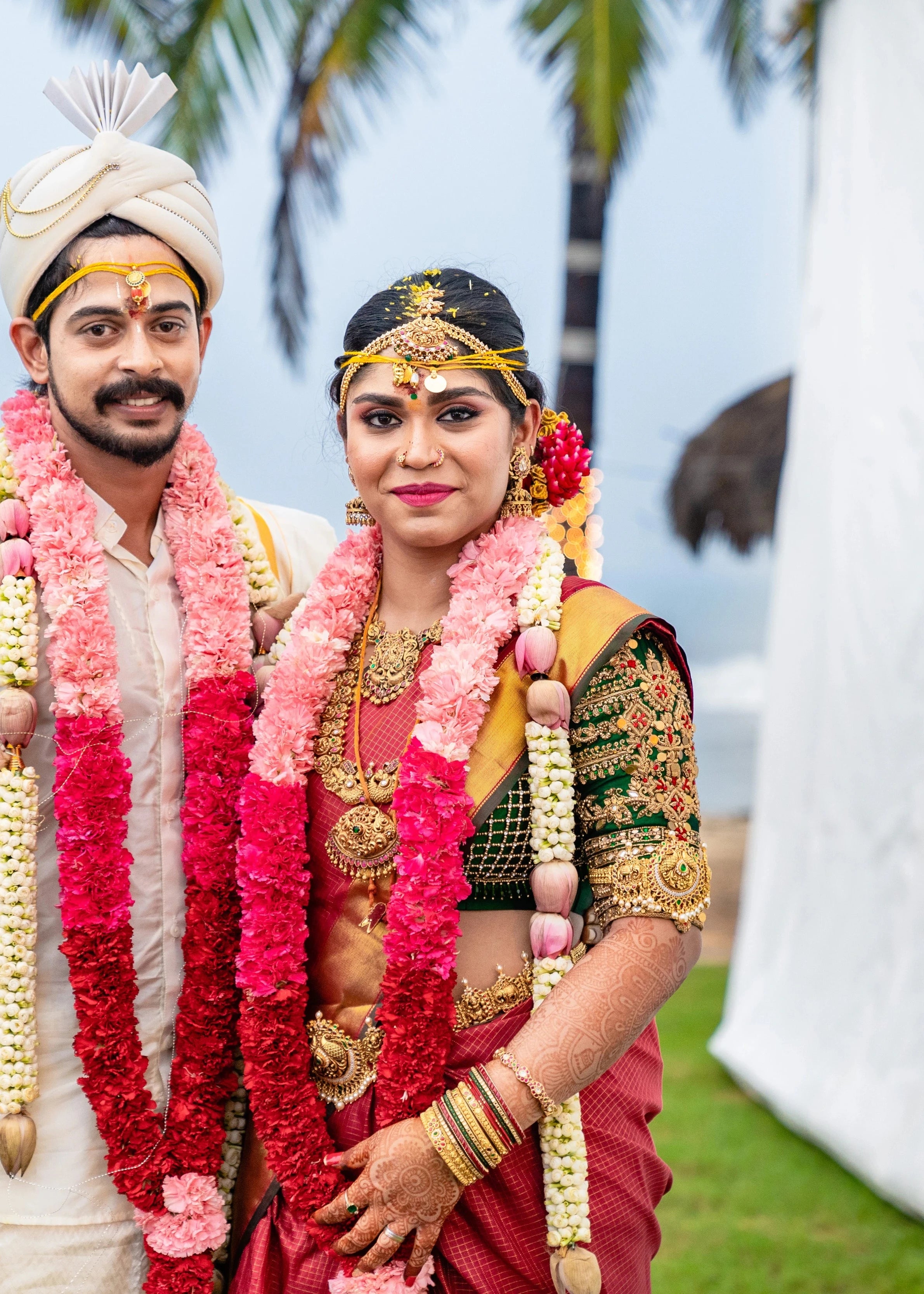 Bride Vidya D posing with groom in a bottle green silk blouse, handcrafted with beads, zardozi, kundan, resham, stones and coins by team Archana Karthick.