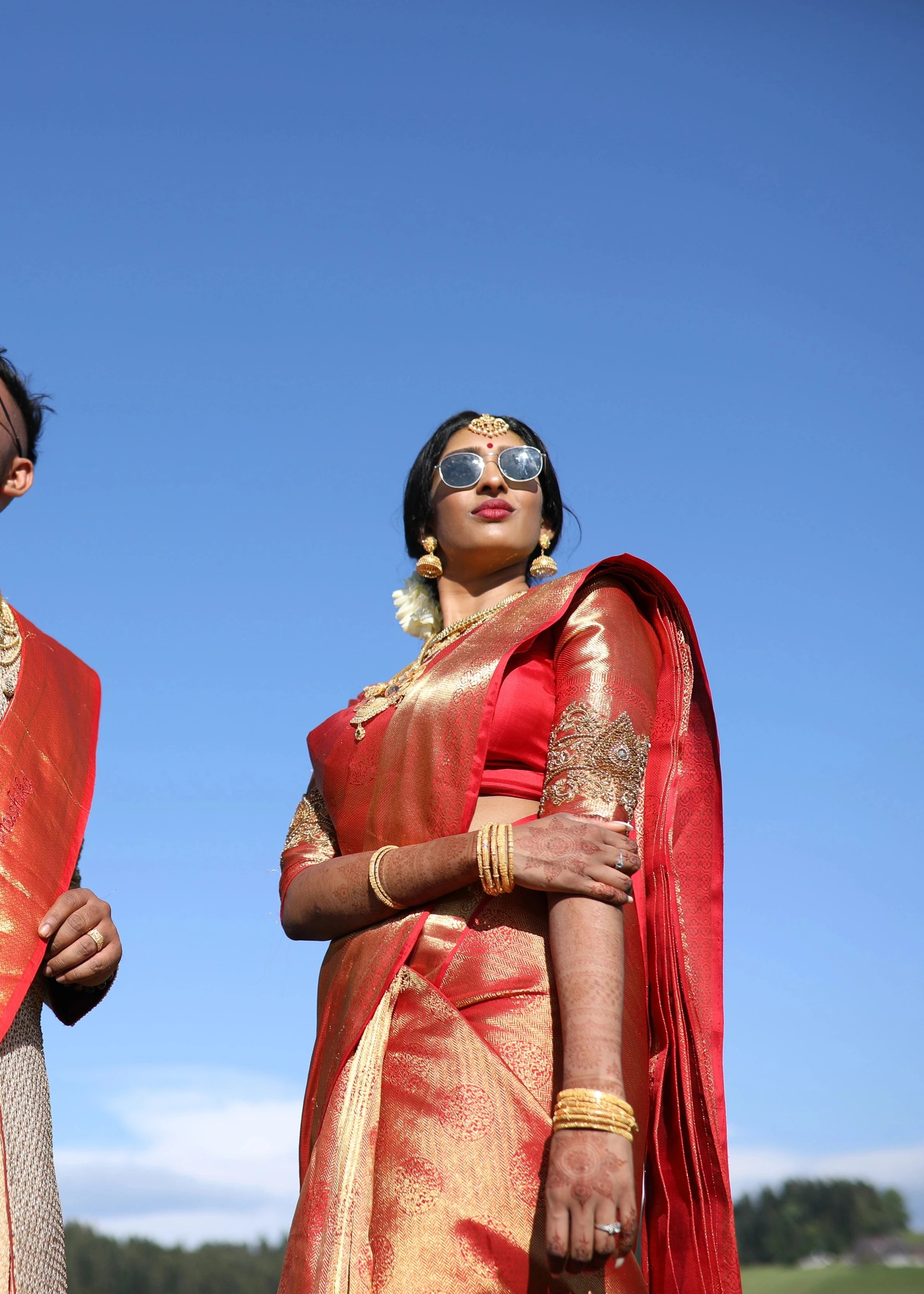 Bride Vithusika from Switzerland posing with sunglasses in a red silk concept blouse for her wedding, handcrafted with zardozi, beads, sequins and cutdana by team Archana Karthick.