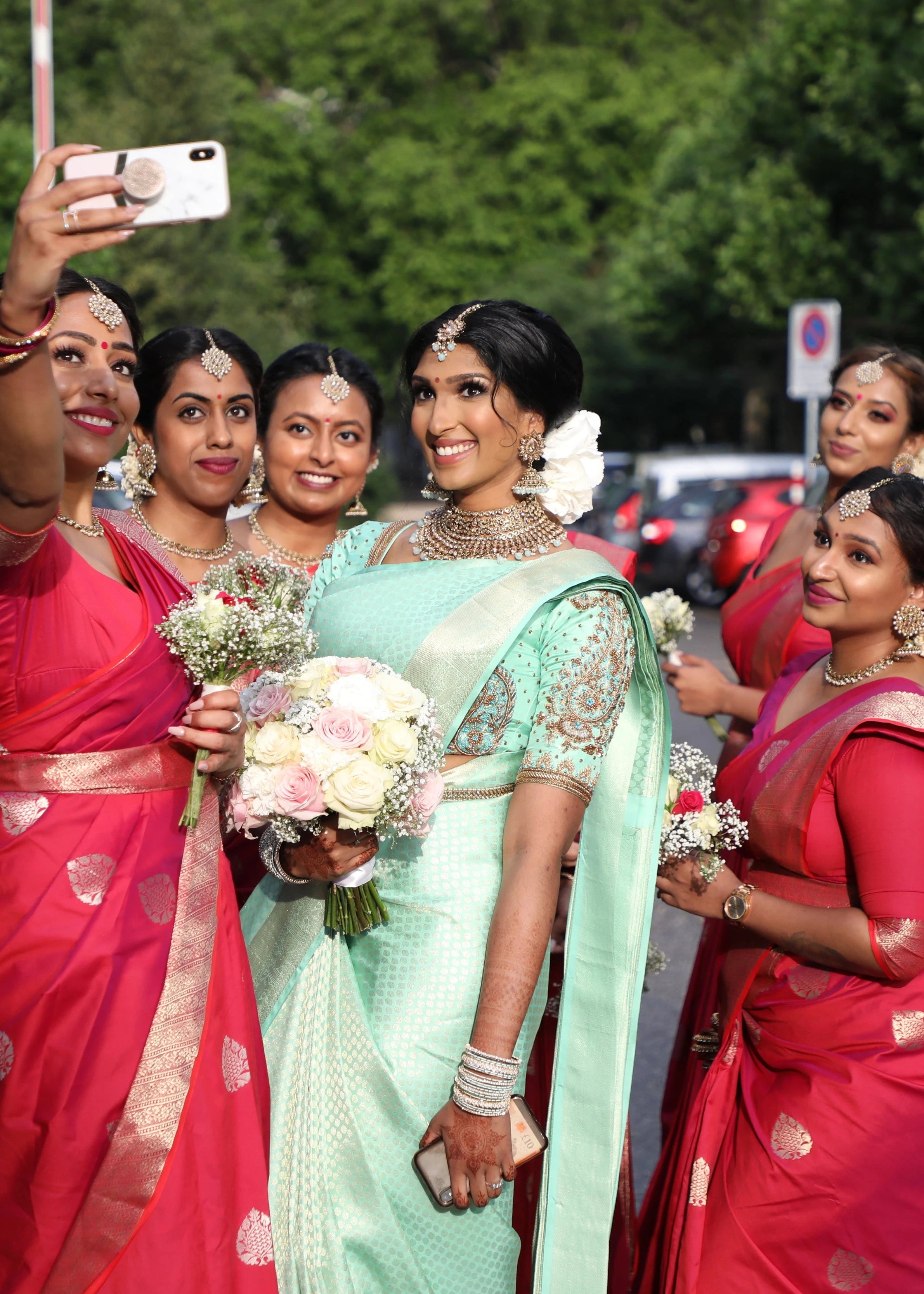 Bride Vithusika from Switzerland taking selfies with bridesmaids in an aquamarine silk concept blouse for her engagement, handcrafted by team Archana Karthick.