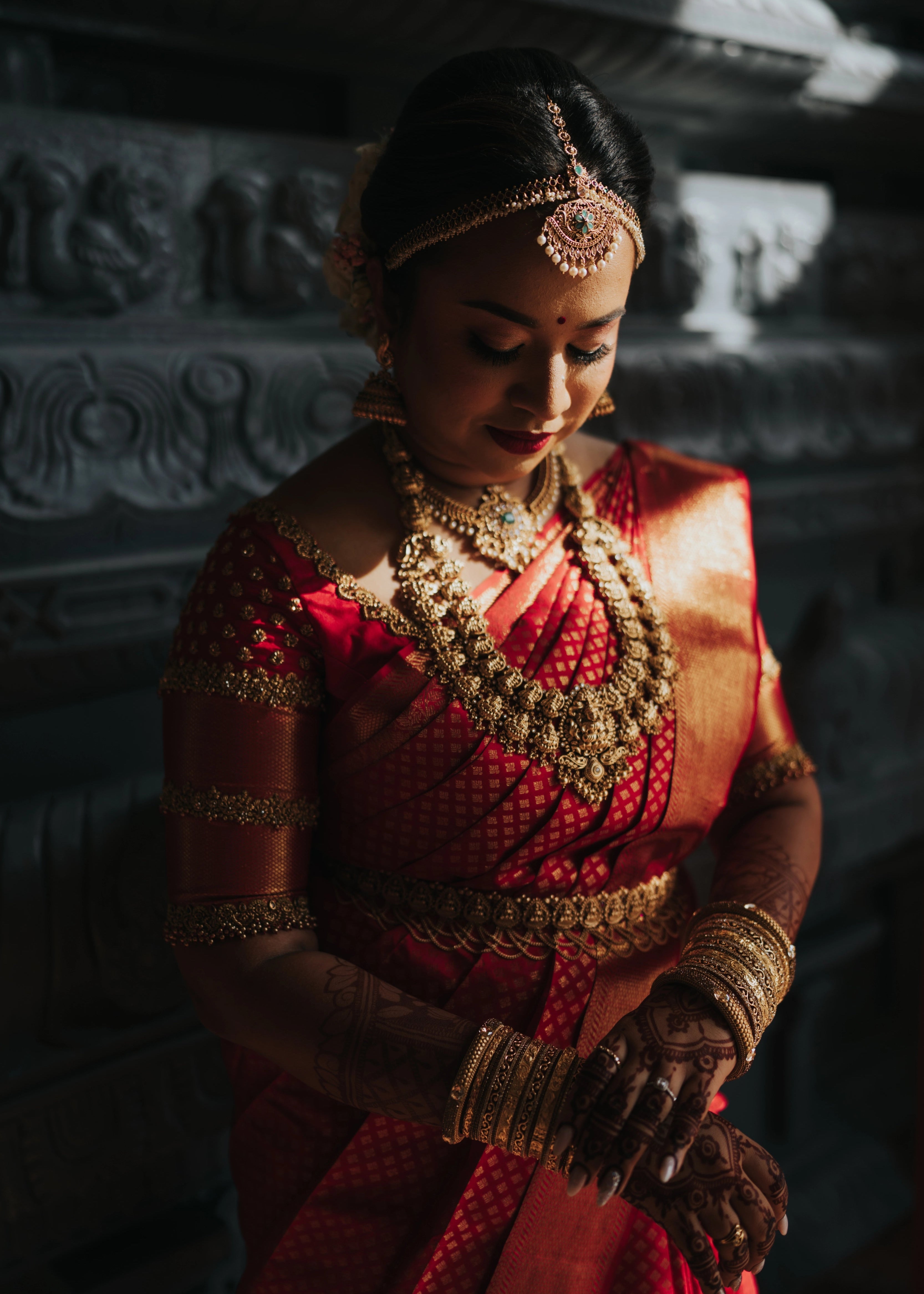 Bride adjusting bangles in a handcrafted palanquin concept red silk blouse features zardozi and beads. Designed by Archana Karthick.