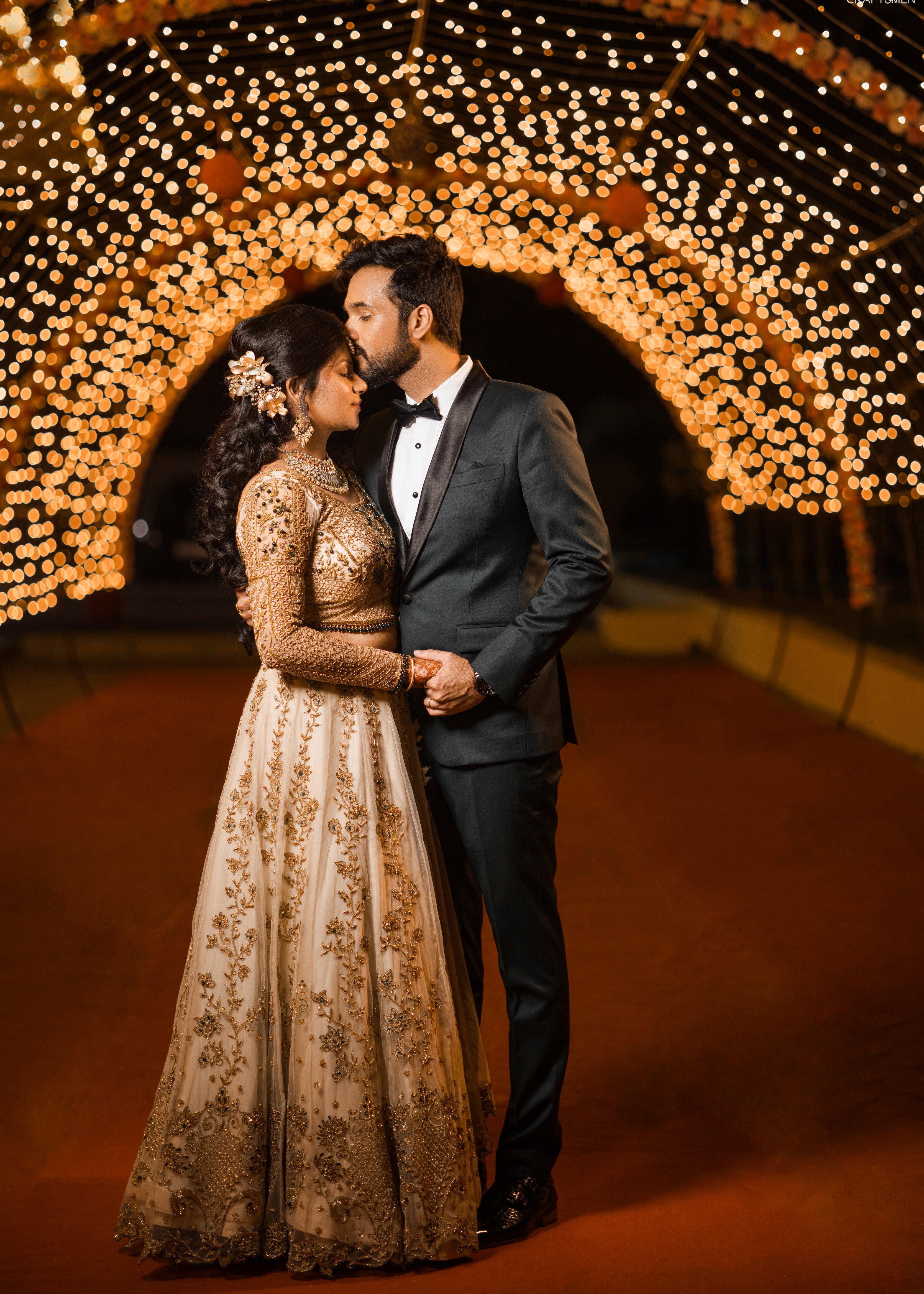 Bride embracing groom in an ivory lehenga in tulle with cut worked dupatta and handcrafted intricately with stones, zardozi, reshams knot work, beads and cutdanas. Designed by Archana Karthick
