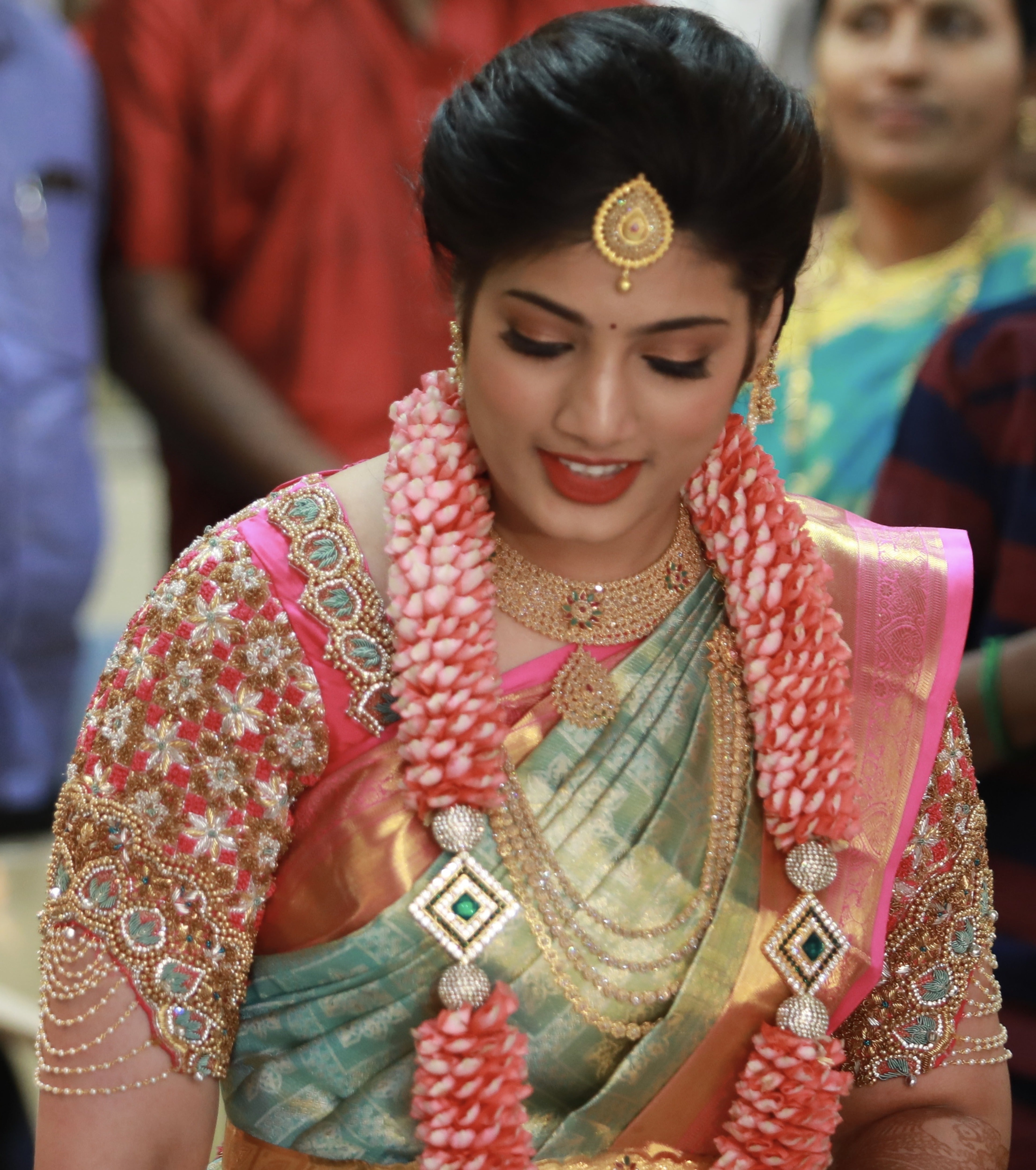 Bride for her engagement in pink raw silk blouse designed by Archana Karthick. Bride is looking down in a shy manner. She also has her garland of pink flowers on her.