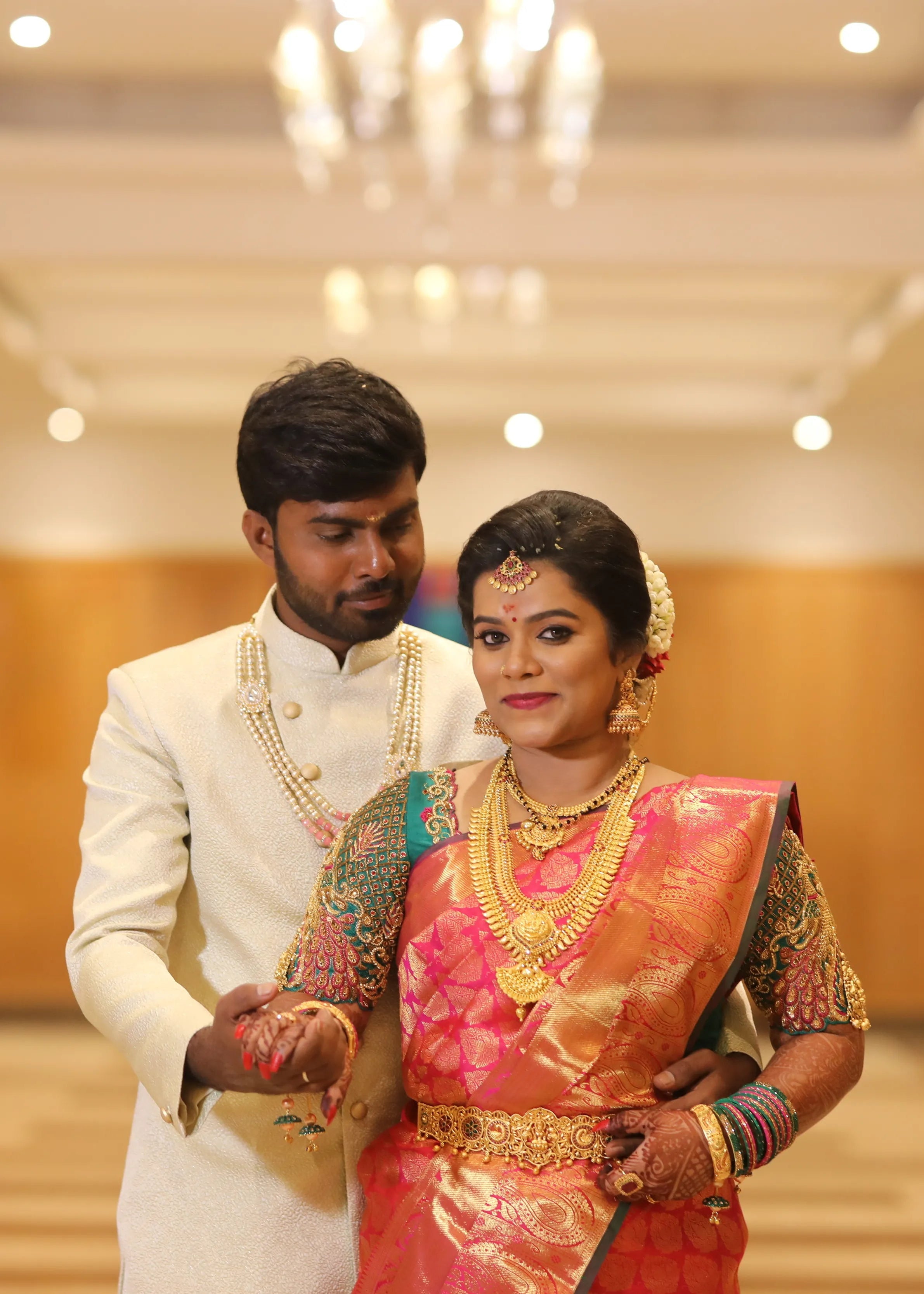Bride from Chennai holding groom's hand in a handcrafted peacock concept green silk blouse with goddess pendants on sleeves. Designed by Archana Karthick