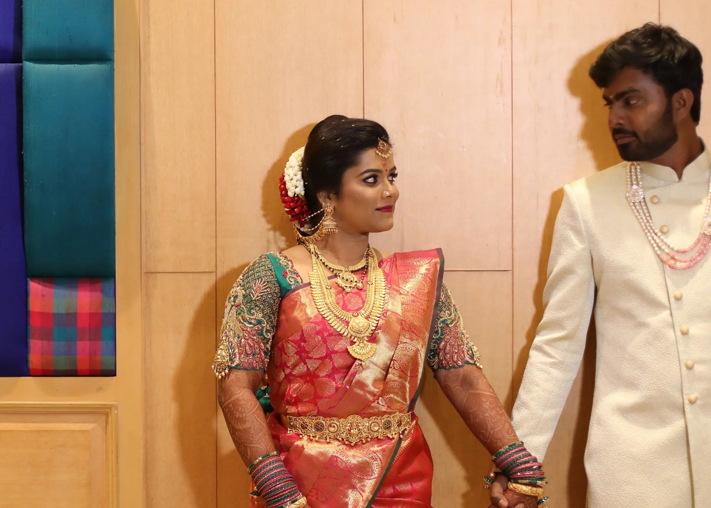 Bride from Chennai holding hands in a handcrafted peacock concept green silk blouse with goddess pendants on sleeves. Designed by Archana Karthick