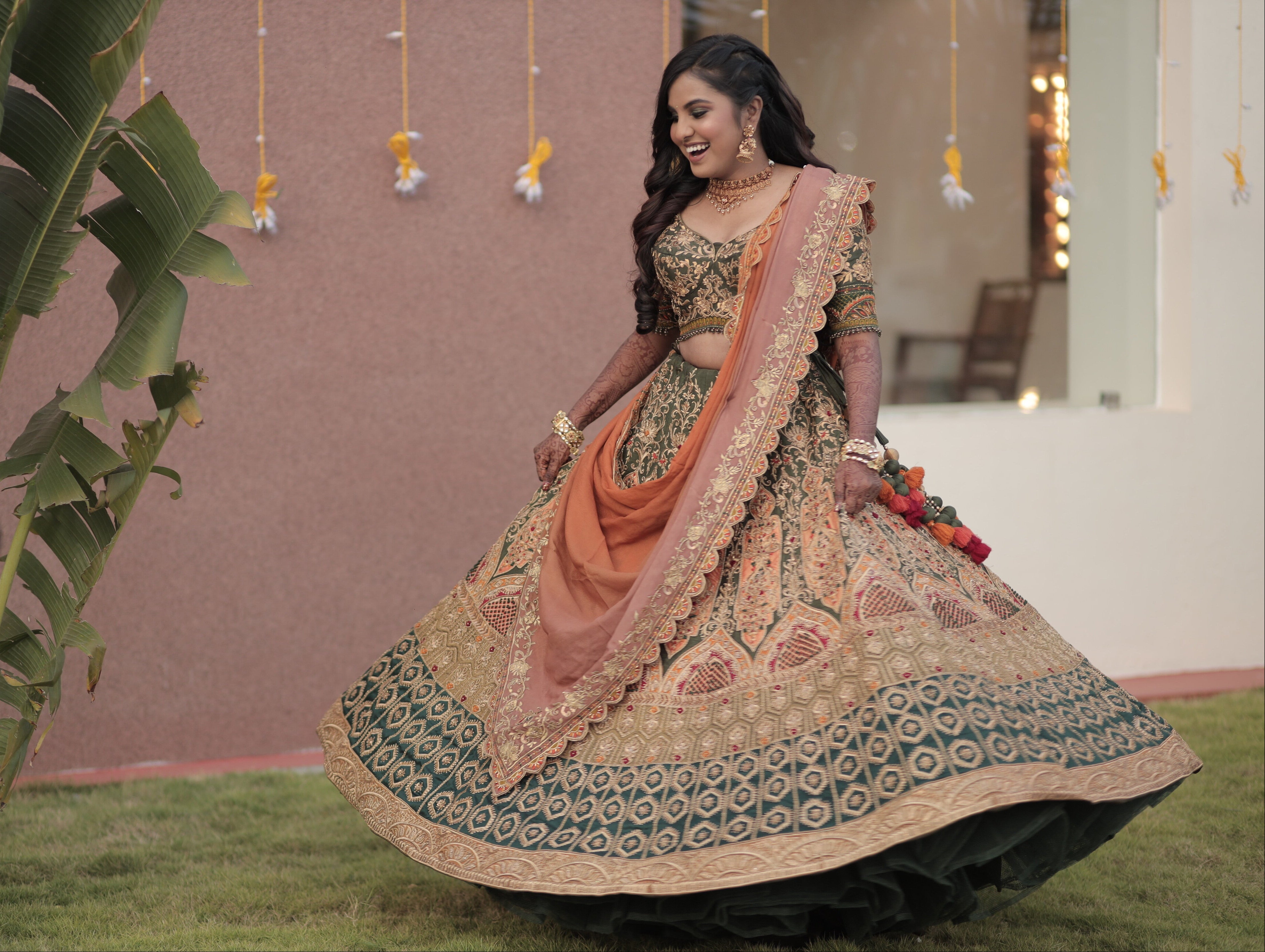 Bride from Chennai laughing in an olive green raw silk lehenga with hints of burnt orange handcrafted intricately with zardozi, crystal beads, resham knot work, cutdanas and sequins. Designed by Archana Karthick.