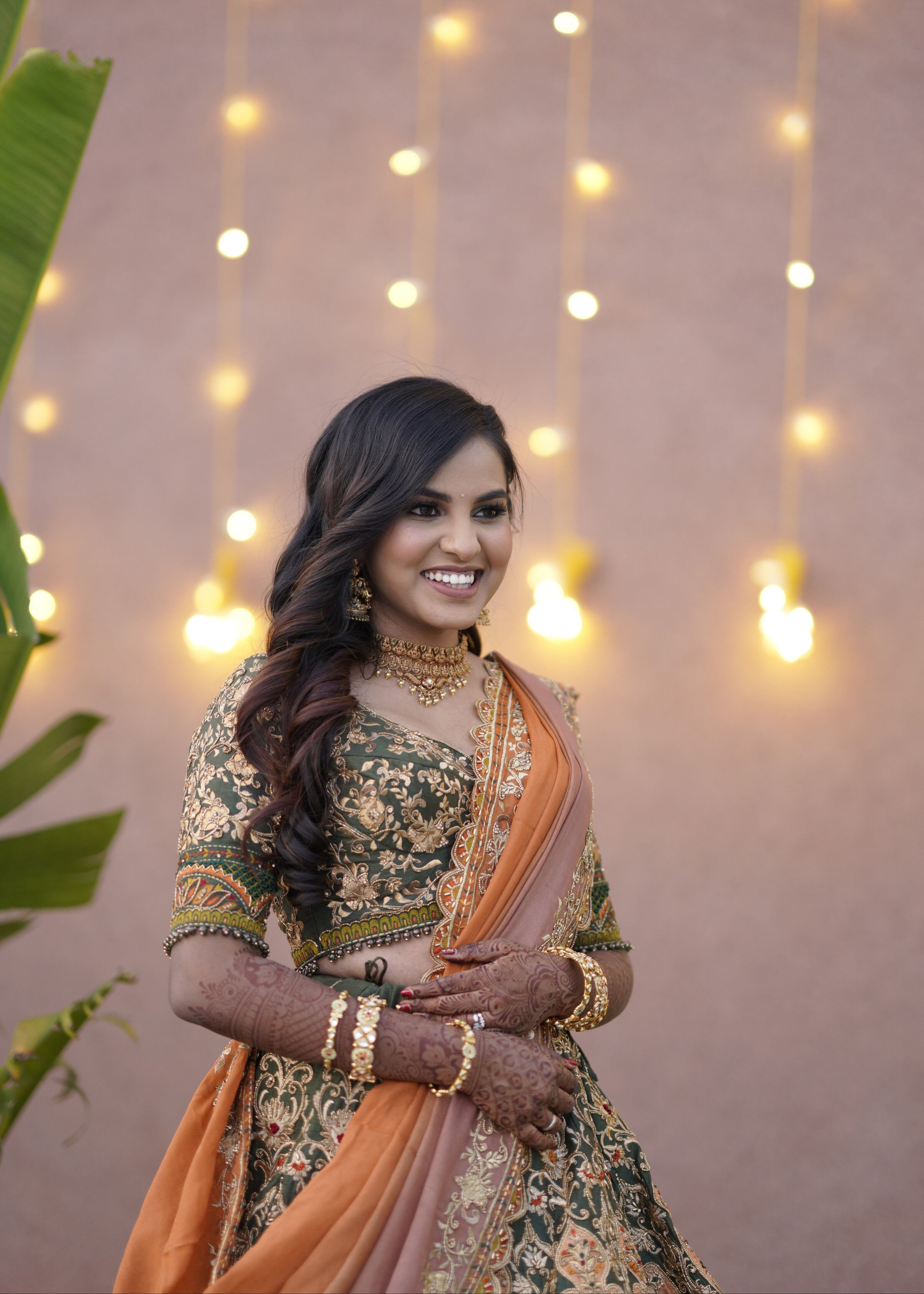 Bride from Chennai looking sideways in an olive green raw silk lehenga with hints of burnt orange handcrafted intricately with zardozi, crystal beads, resham knot work, cutdanas and sequins. Designed by Archana Karthick.