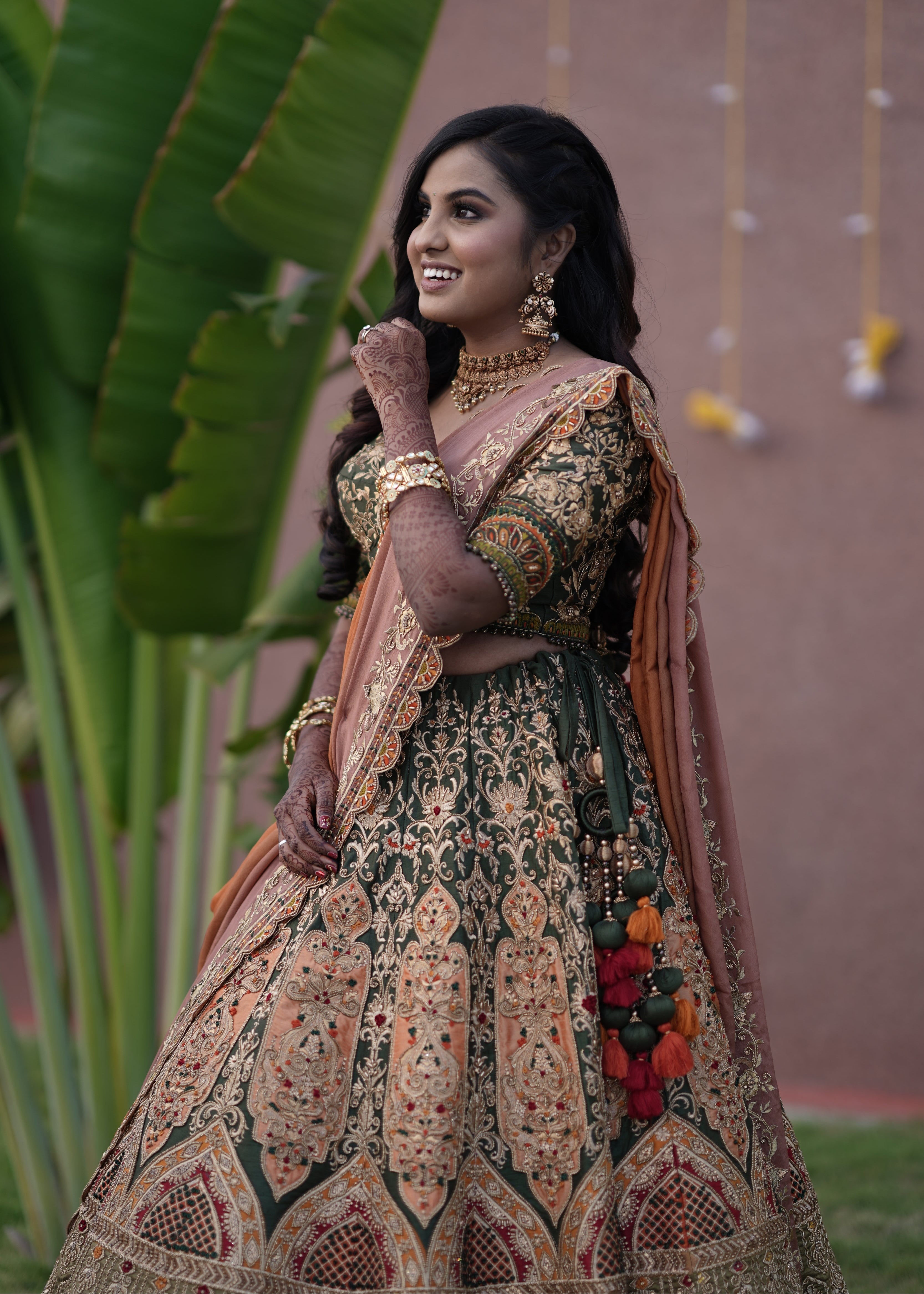 Bride from Chennai looking up in an olive green raw silk lehenga with hints of burnt orange handcrafted intricately with zardozi, crystal beads, resham knot work, cutdanas and sequins. Designed by Archana Karthick.