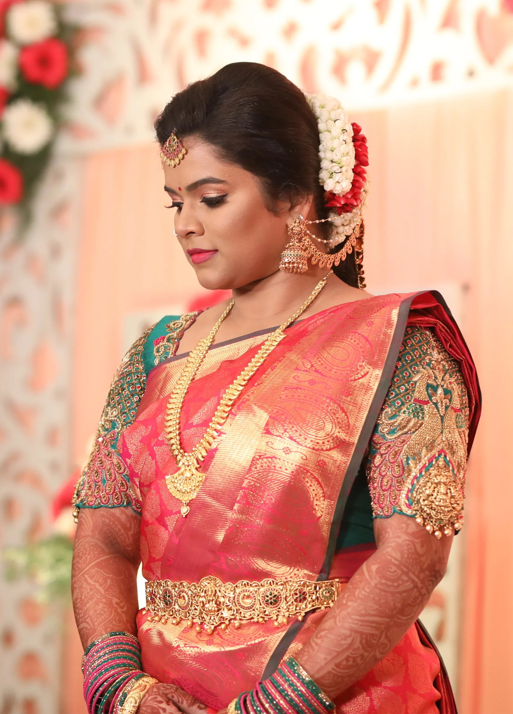 Bride from Chennai posing in a handcrafted peacock concept green silk blouse with goddess pendants on sleeves. Designed by Archana Karthick
