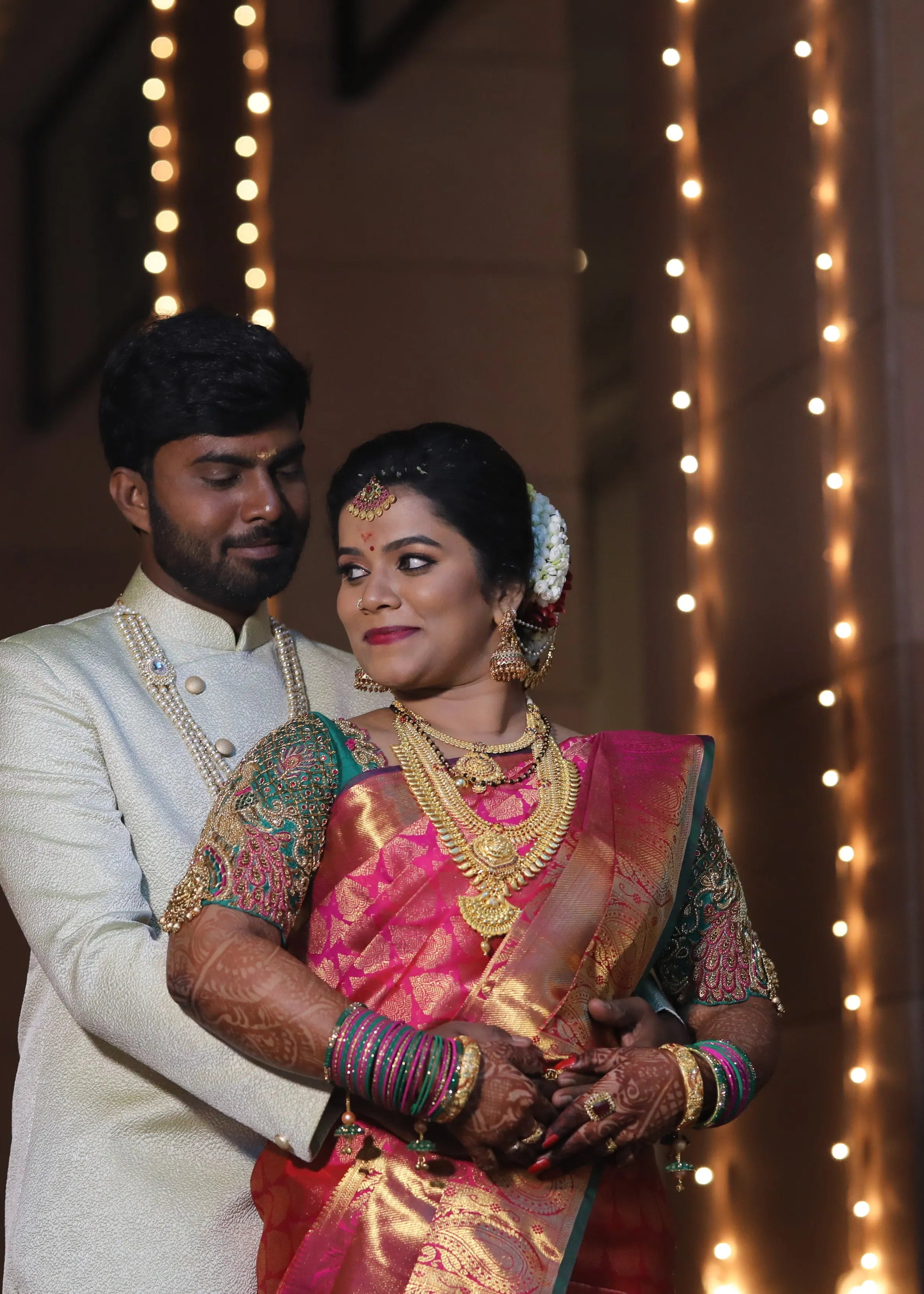 Bride from Chennai posing with groom in a handcrafted peacock concept green silk blouse with goddess pendants on sleeves. Designed by Archana Karthick