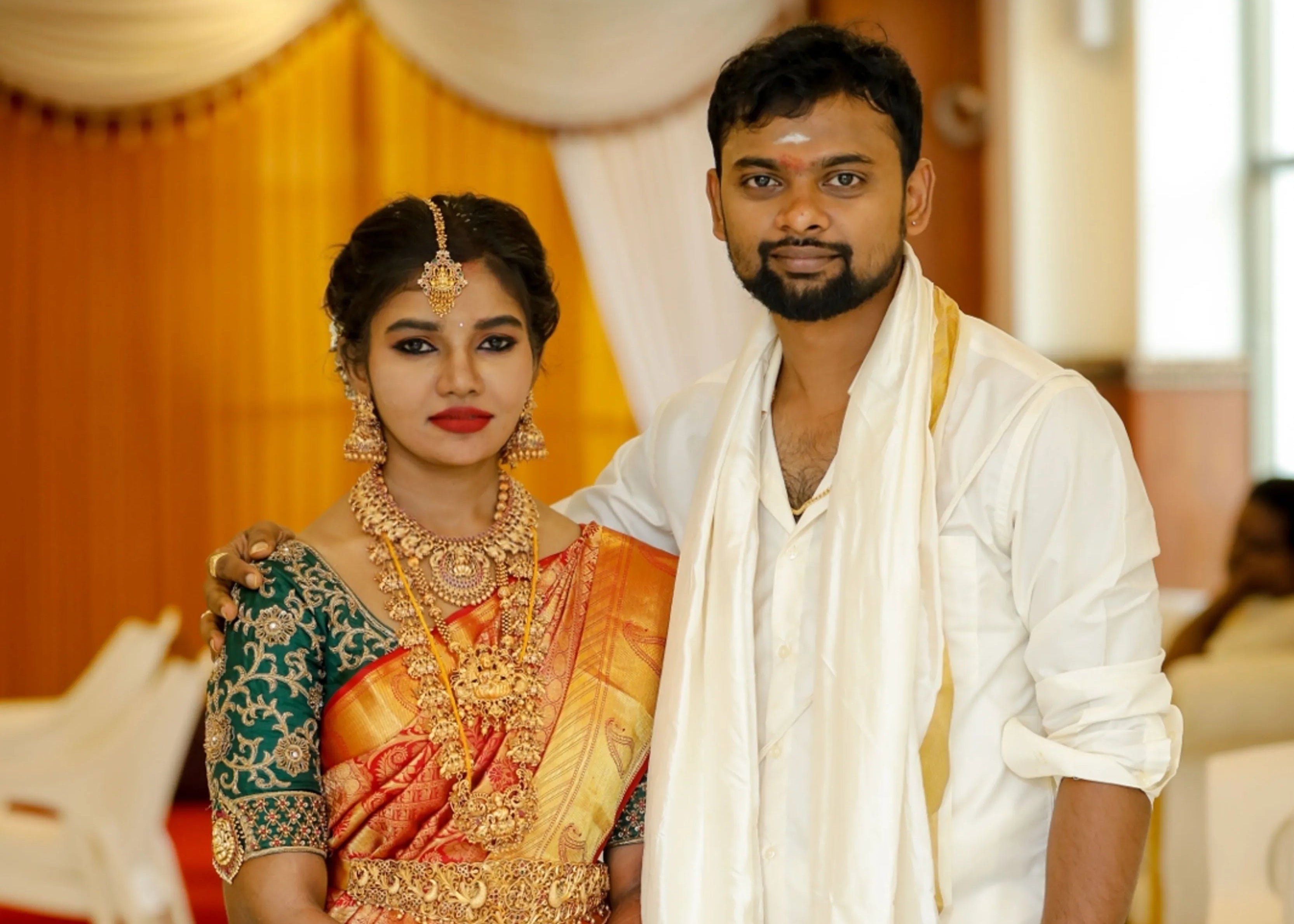 Bride from Chennai posing with groom in bottle green silk blouse embellished with zardozi and goddess pendants on sleeves.