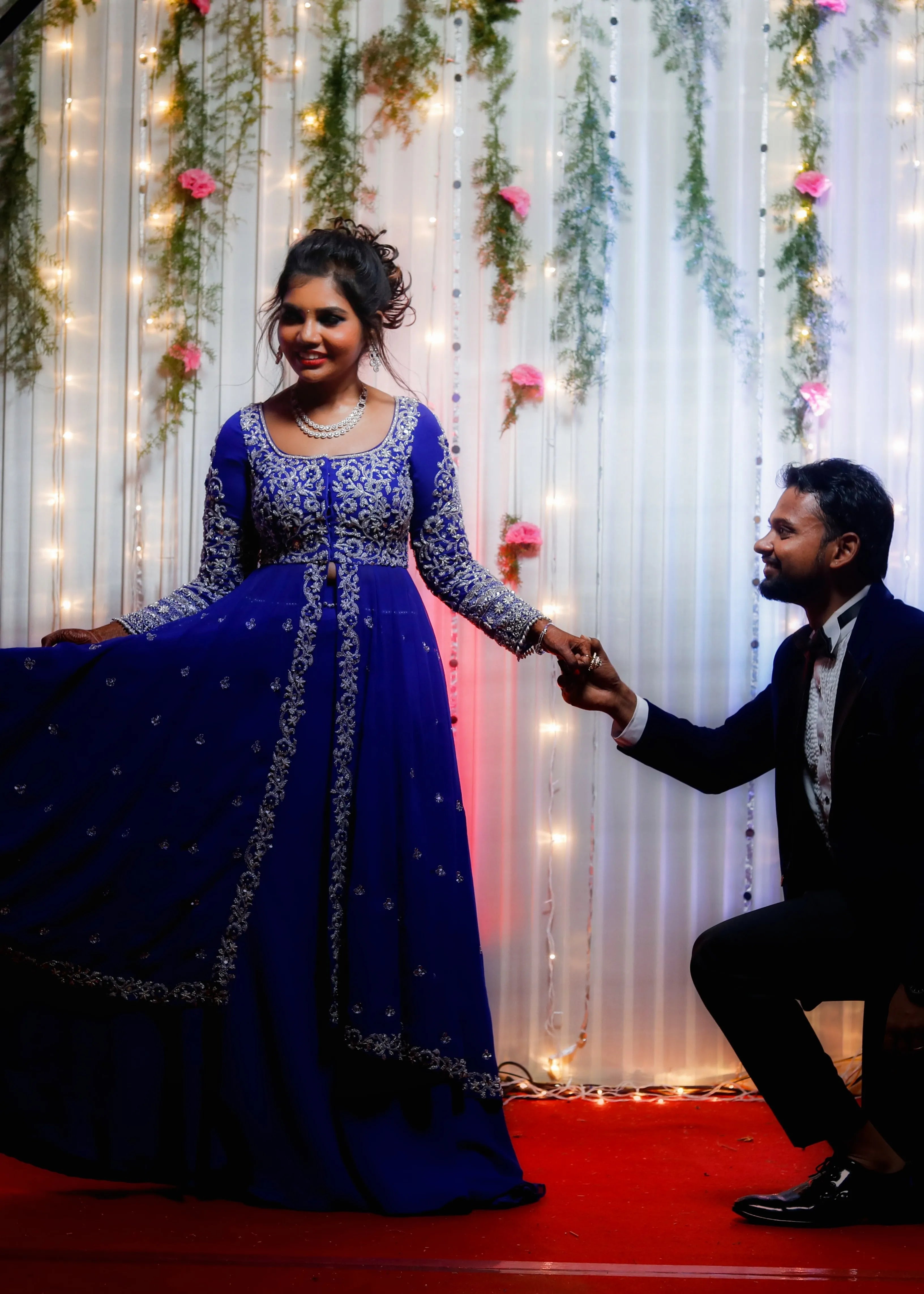 Bride from Chennai posing with groom on stage in navy blue masakali lehenga with silver embellishments designed by Archana Karthick