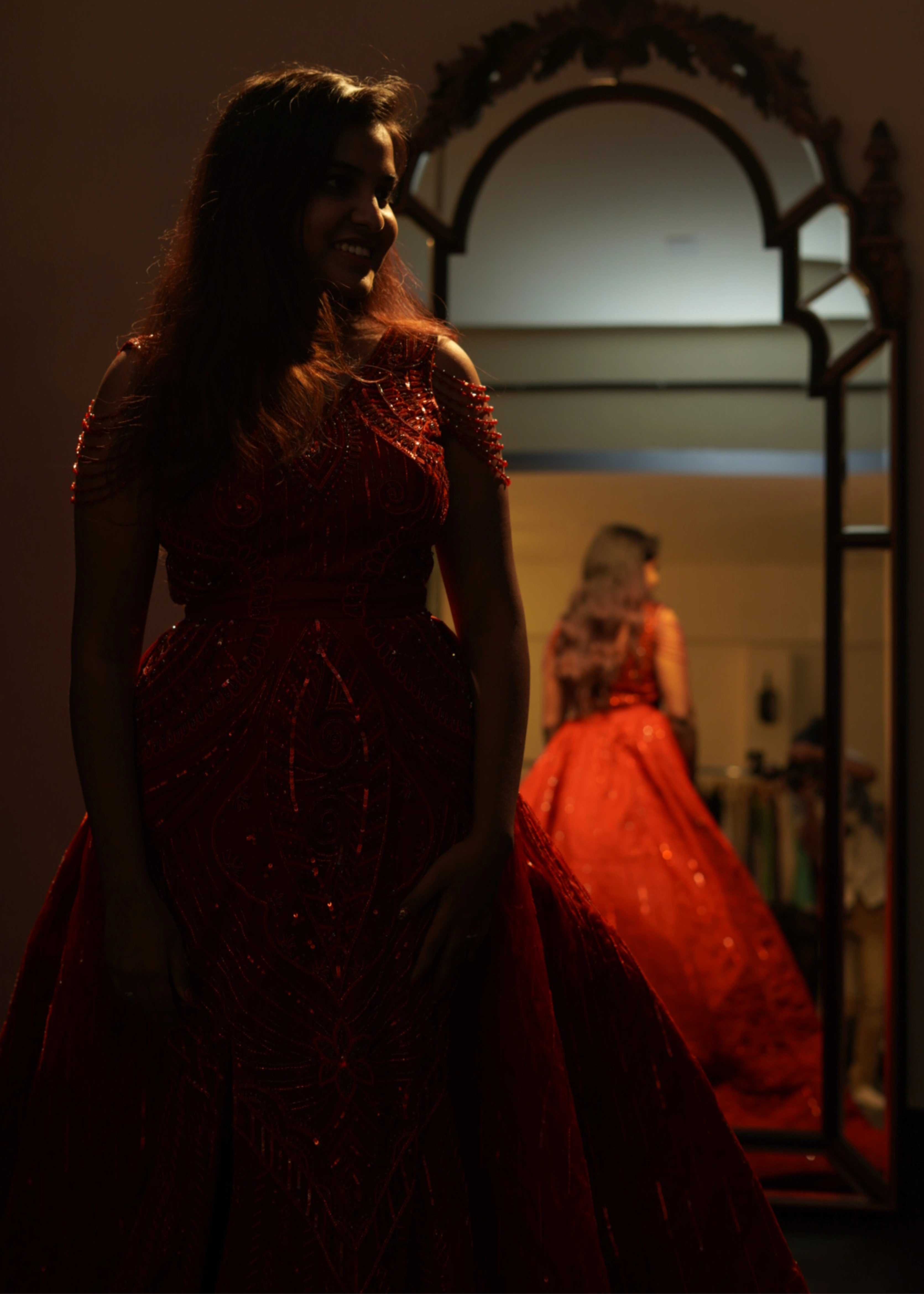 Bride from Chennai smiling in a red mermaid gown with detachable trail handcrafted with rhinestones, crystal beads, cutdanas and sequins. Designed by Archana Karthick