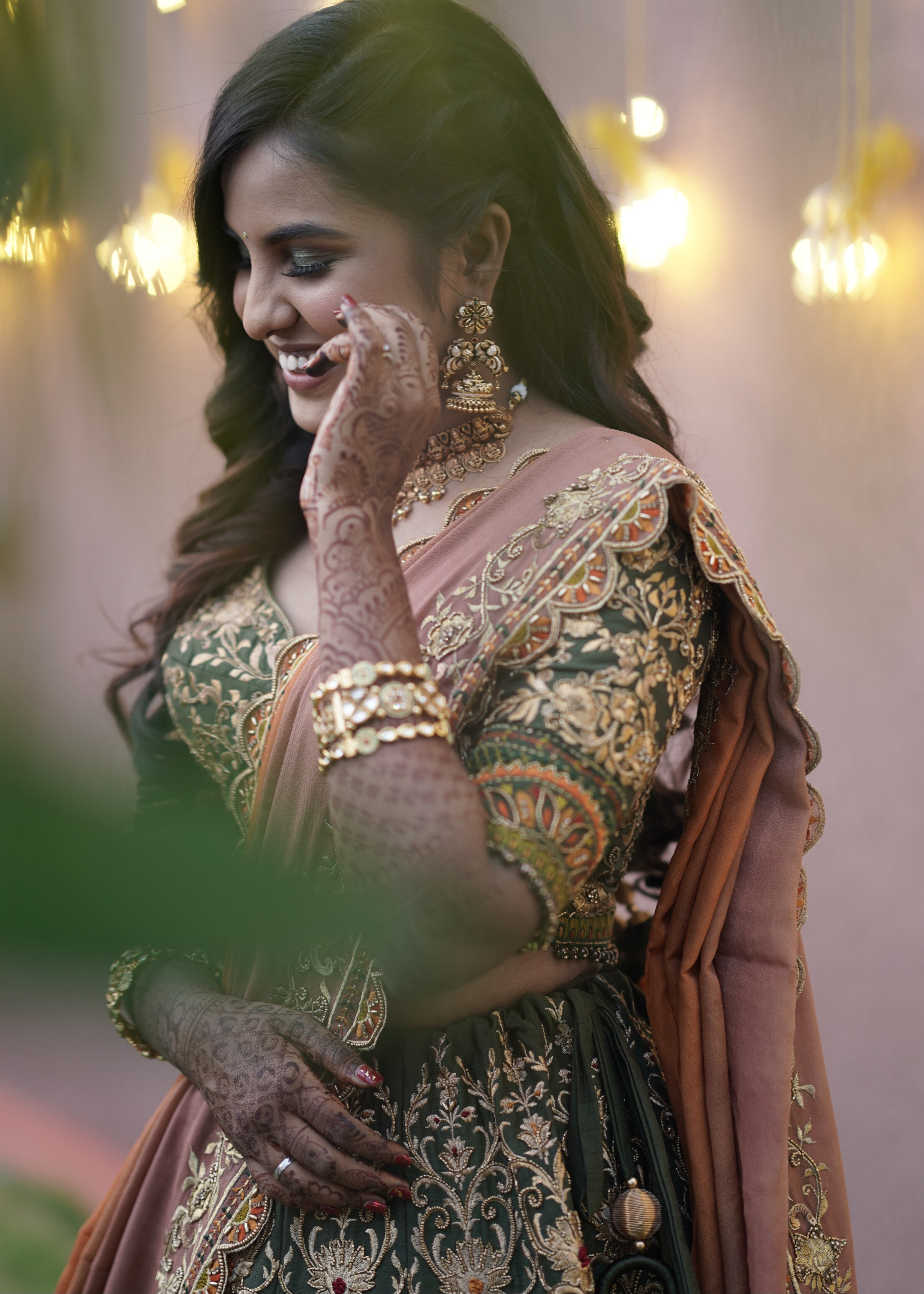 Bride from Chennai smiling in an olive green raw silk lehenga with hints of burnt orange handcrafted intricately with zardozi, crystal beads, resham knot work, cutdanas and sequins. Designed by Archana Karthick.