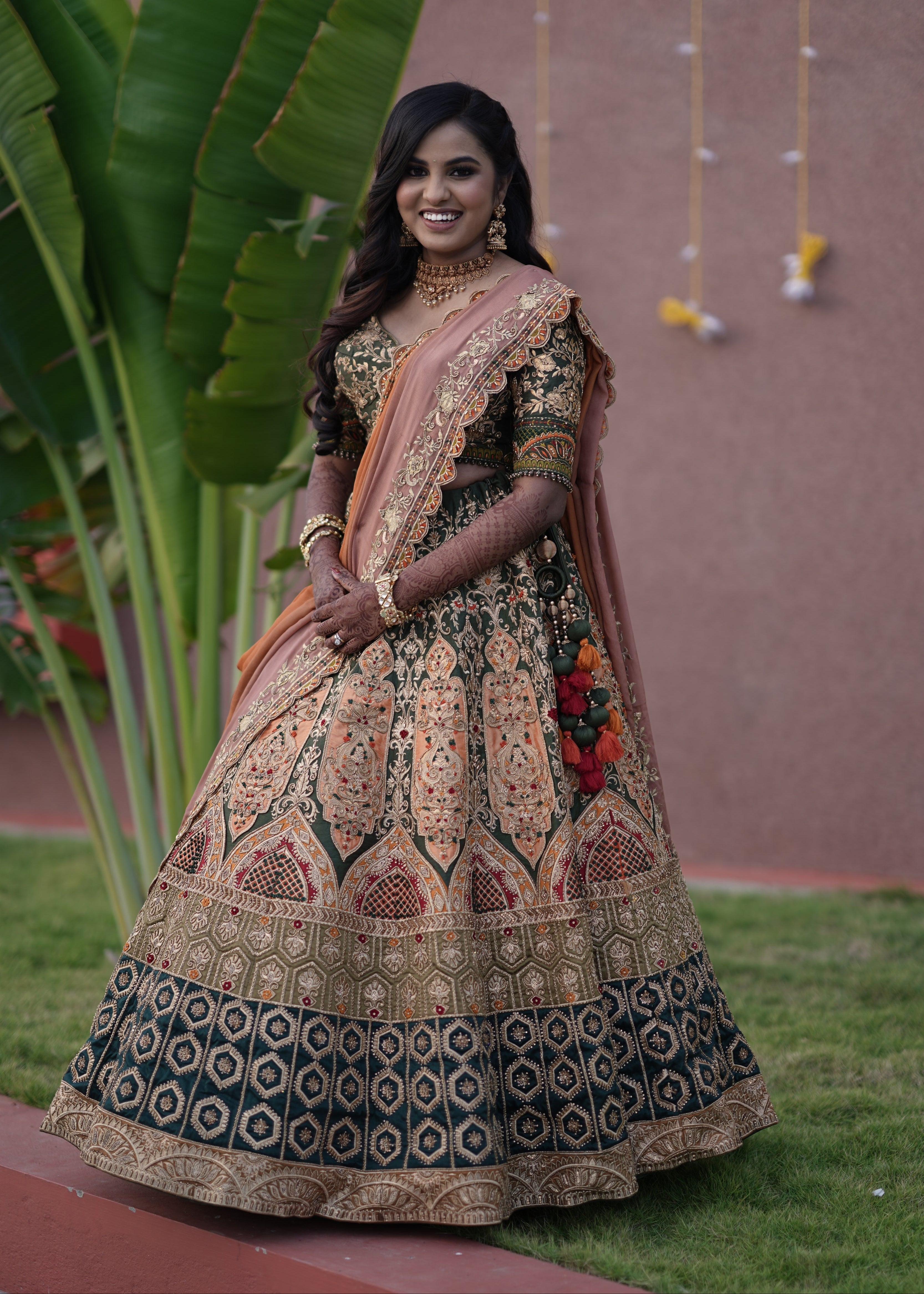Bride from Chennai standing in an olive green raw silk lehenga with hints of burnt orange handcrafted intricately with zardozi, crystal beads, resham knot work, cutdanas and sequins. Designed by Archana Karthick.