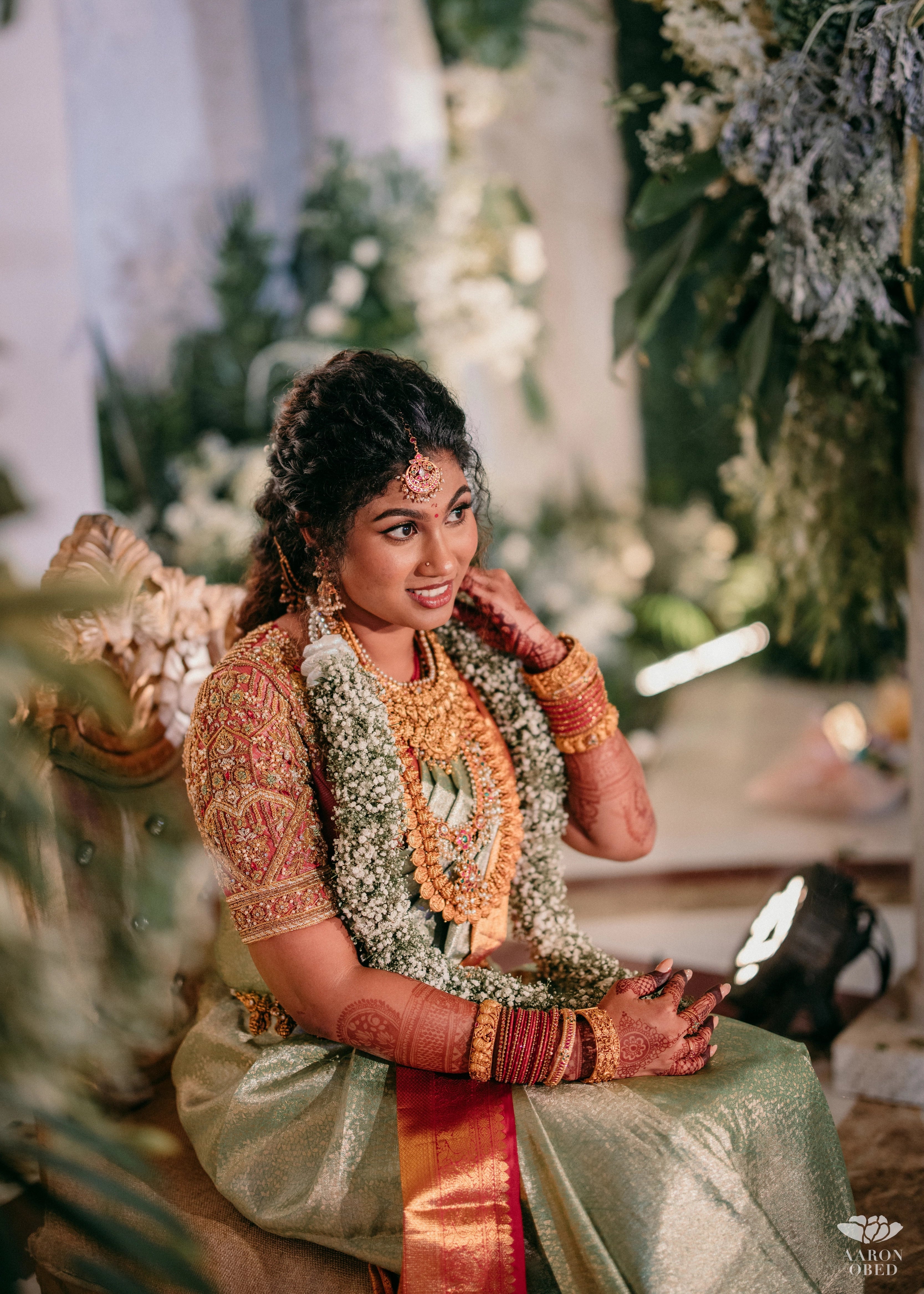 Bride from Chennai with a garland in a concept red silk blouse handcrafted intricately with rhinestones, pearls, zardozi, resham knot work and stones. Designed by Archana Karthick