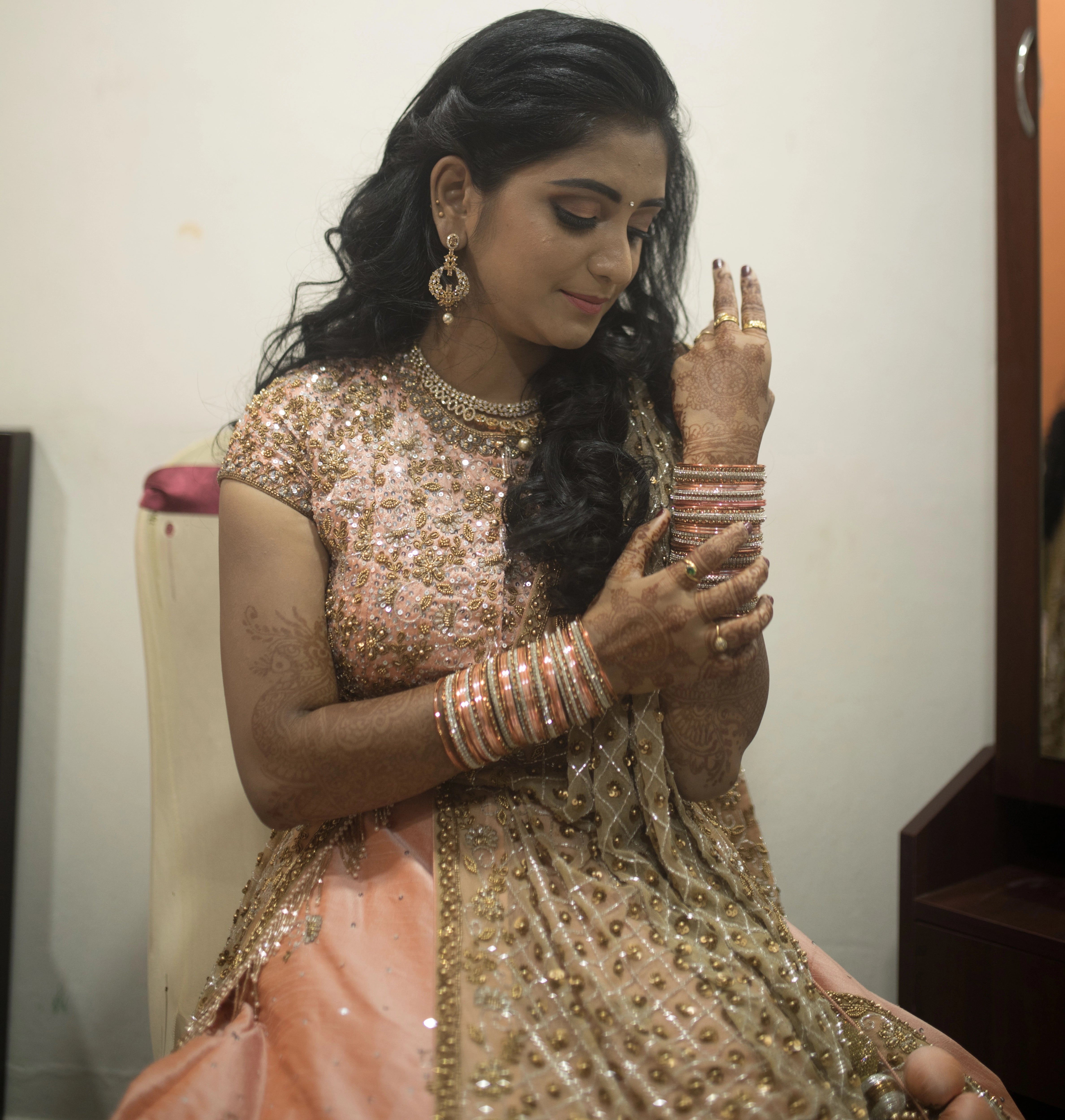 Bride from Coimbatore in a mehendi pose in a peach raw silk lehenga and tulle dupatta handcrafted intricately with beads, sequins, and cutdana by team Archana Karthick.