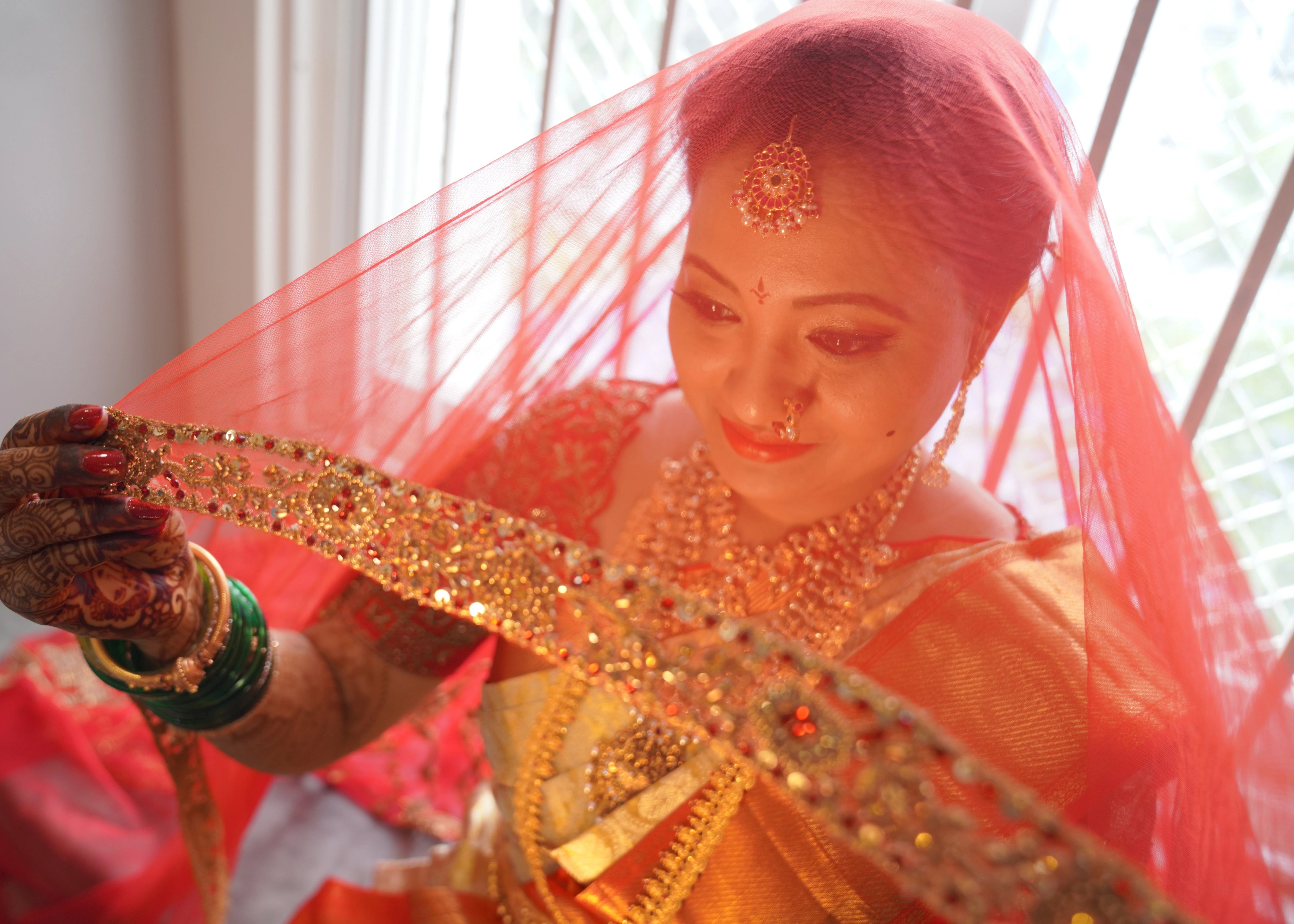 Bride from Seatlle smiling in a concept red raw silk blouse and tulle veil handcrafted intricately with zardozi, beads, stones and sequins. Designed by Archana Karthick