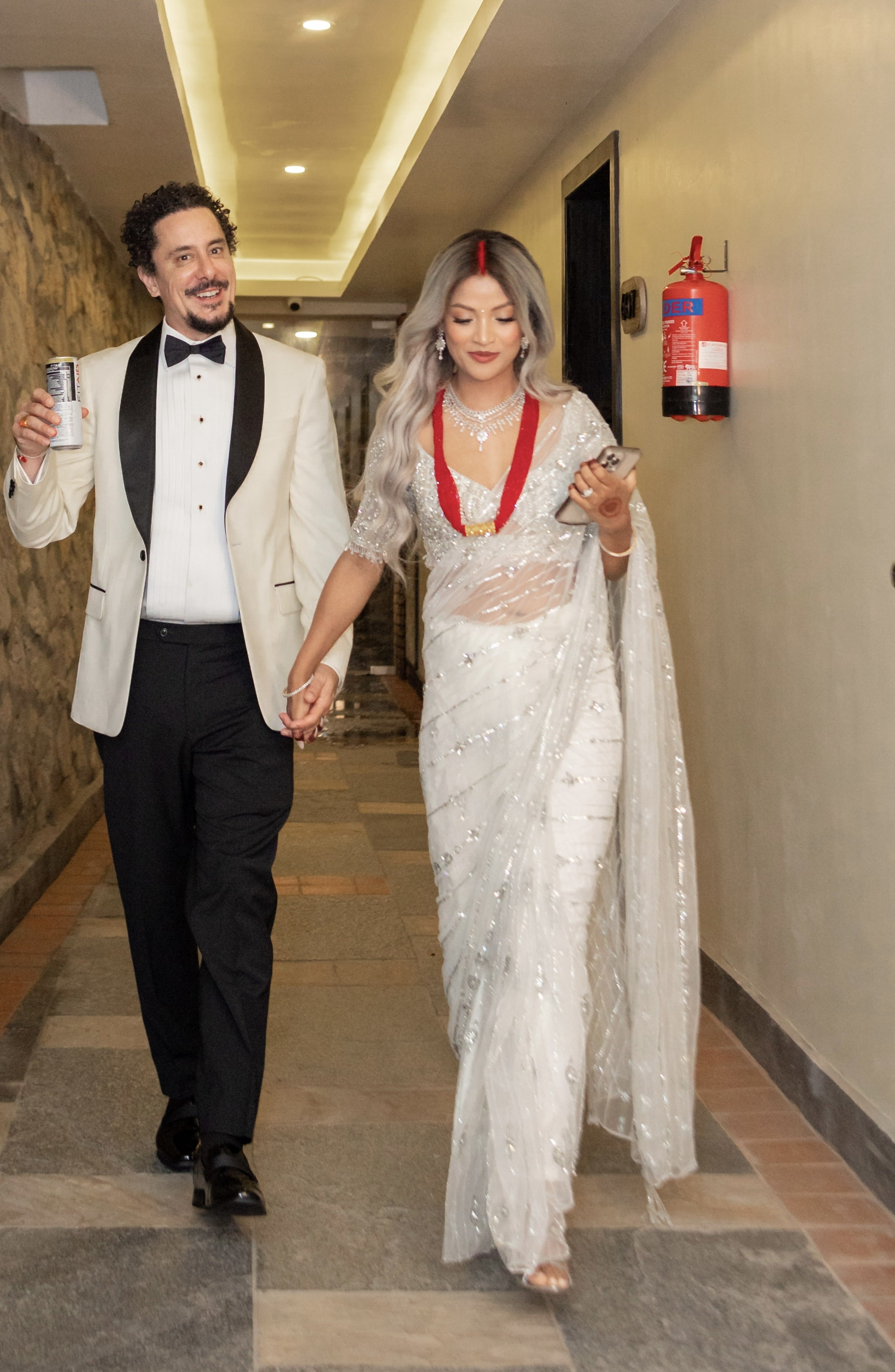 Bride from texas in white net saree for wedding reception in nepal. She is walking hand-in-hand with the groom posing for the photo with a full front view of the lovely white saree.
