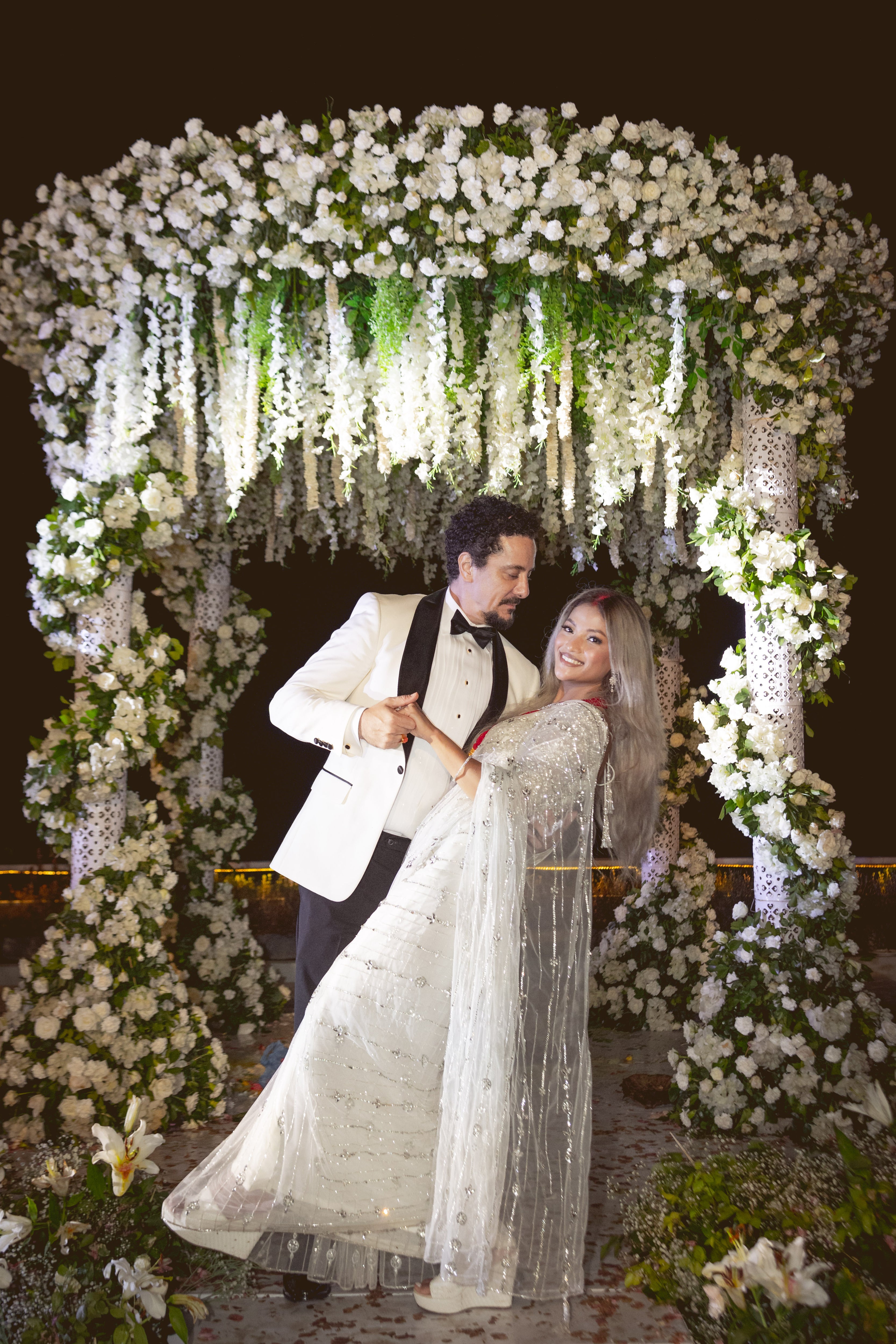 Bride from texas in white net saree for wedding reception in nepal. She leans back in his arms giving us a full side view of the lovely white saree. The saree shines with intricate stonework, sequins and cut dana details.