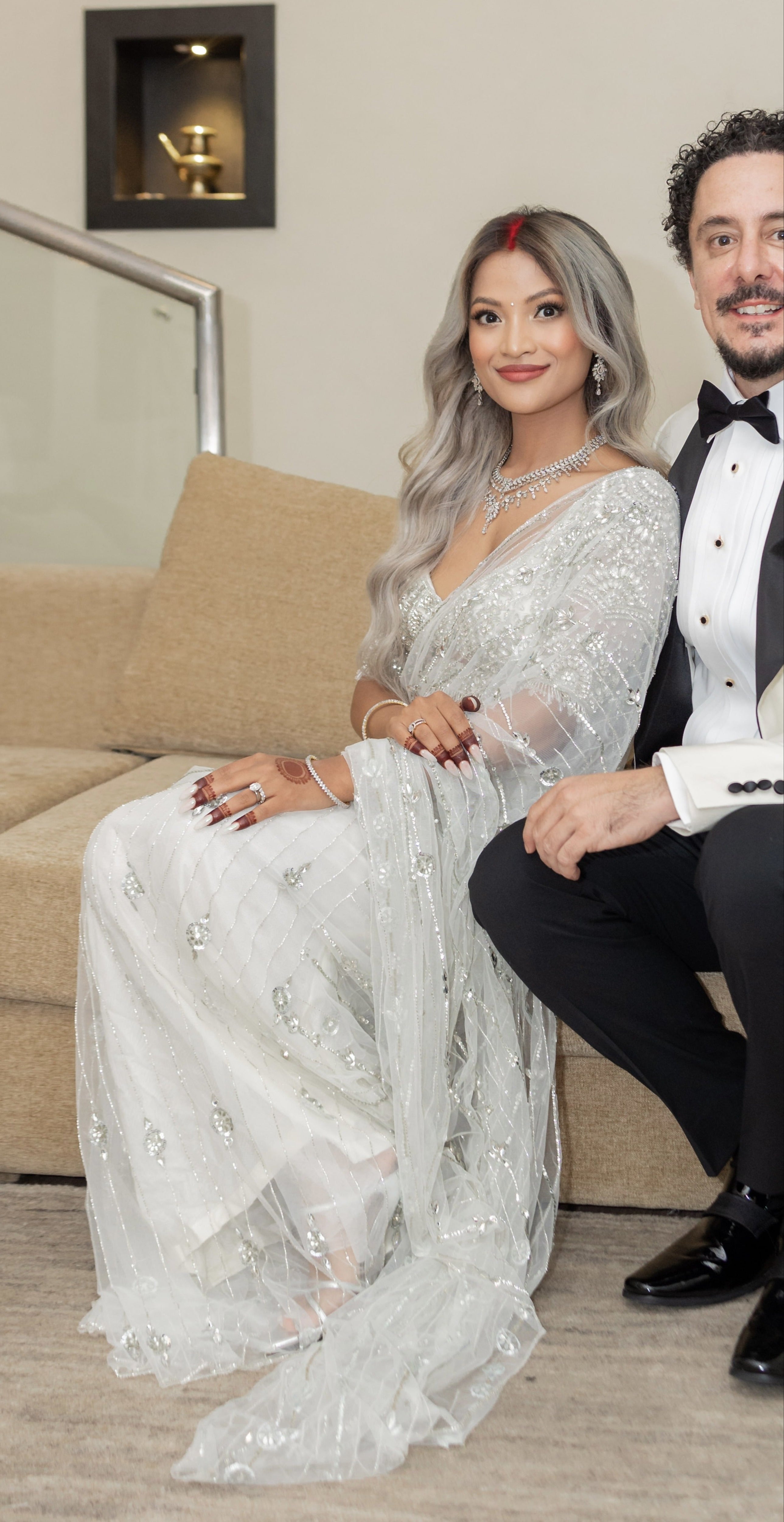 Bride from texas in white net saree for wedding reception in nepal. She looks straight at the camera in this closeup shot where we can see the full side view of the saree and blouse. The saree shines with intricate stonework, sequins and cut dana details.