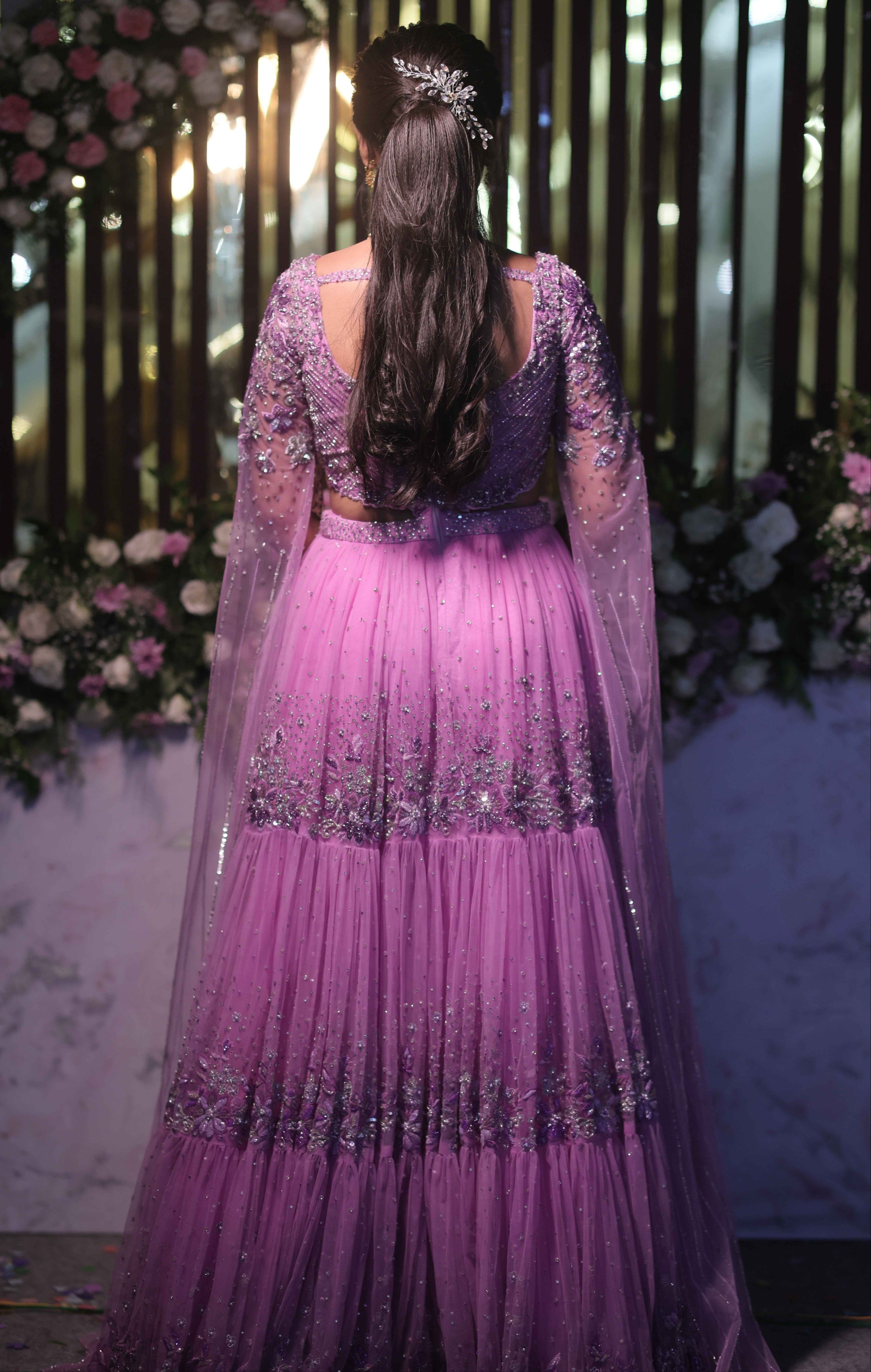 Bride in a lavender handcrafted lehenga with trail sleeves for her reception. The outfits for both the bride and groom is designed by Archana Karthick. Back lehenga design is captured here clearly.