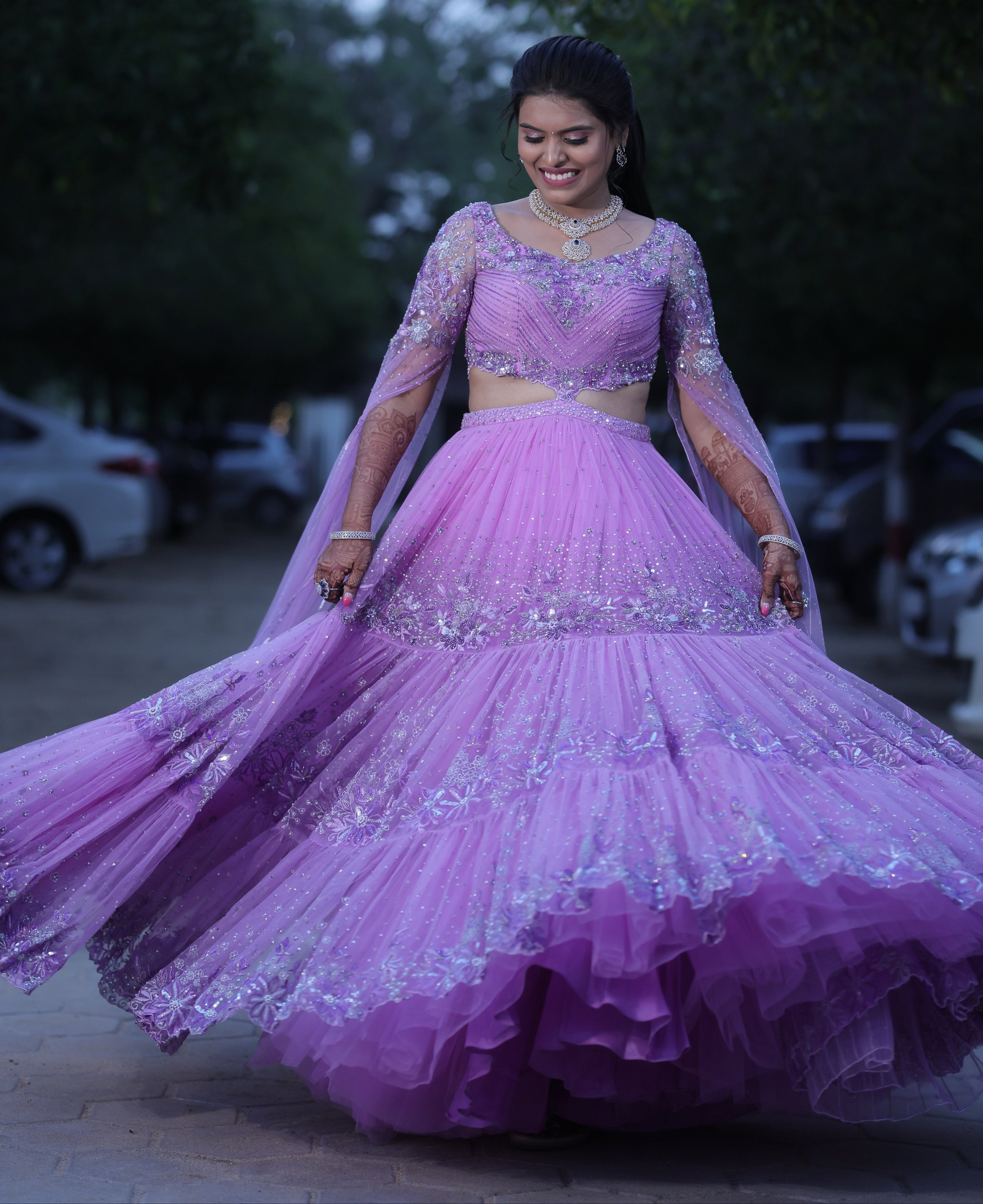 Bride in a lavender handcrafted lehenga with trail sleeves twirling happily for her reception. The outfits for both the bride and groom is designed by Archana Karthick.