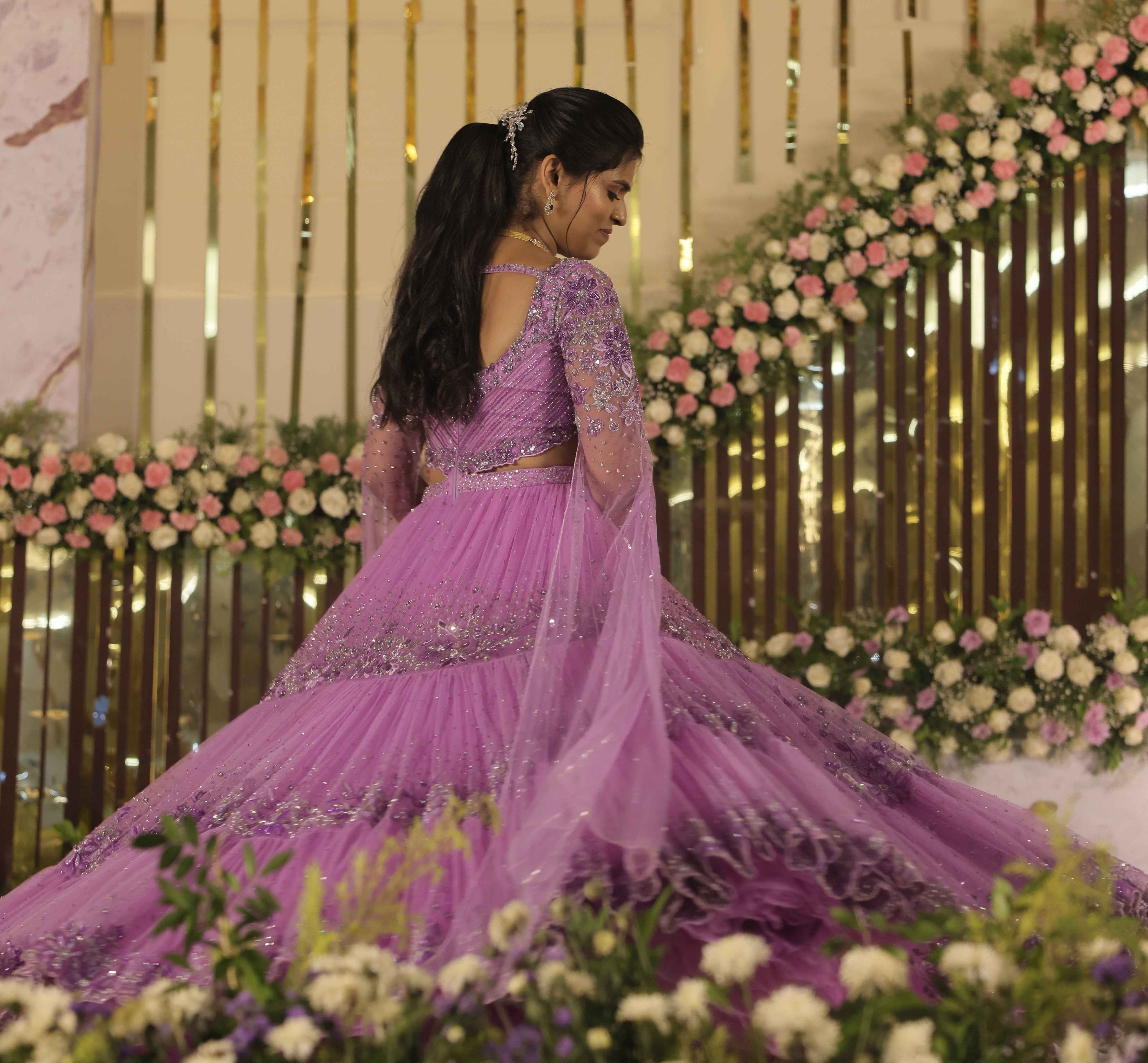 Bride in a lavender handcrafted lehenga with trail sleeves twirling on stage for her reception. The outfits for both the bride and groom is designed by Archana Karthick.