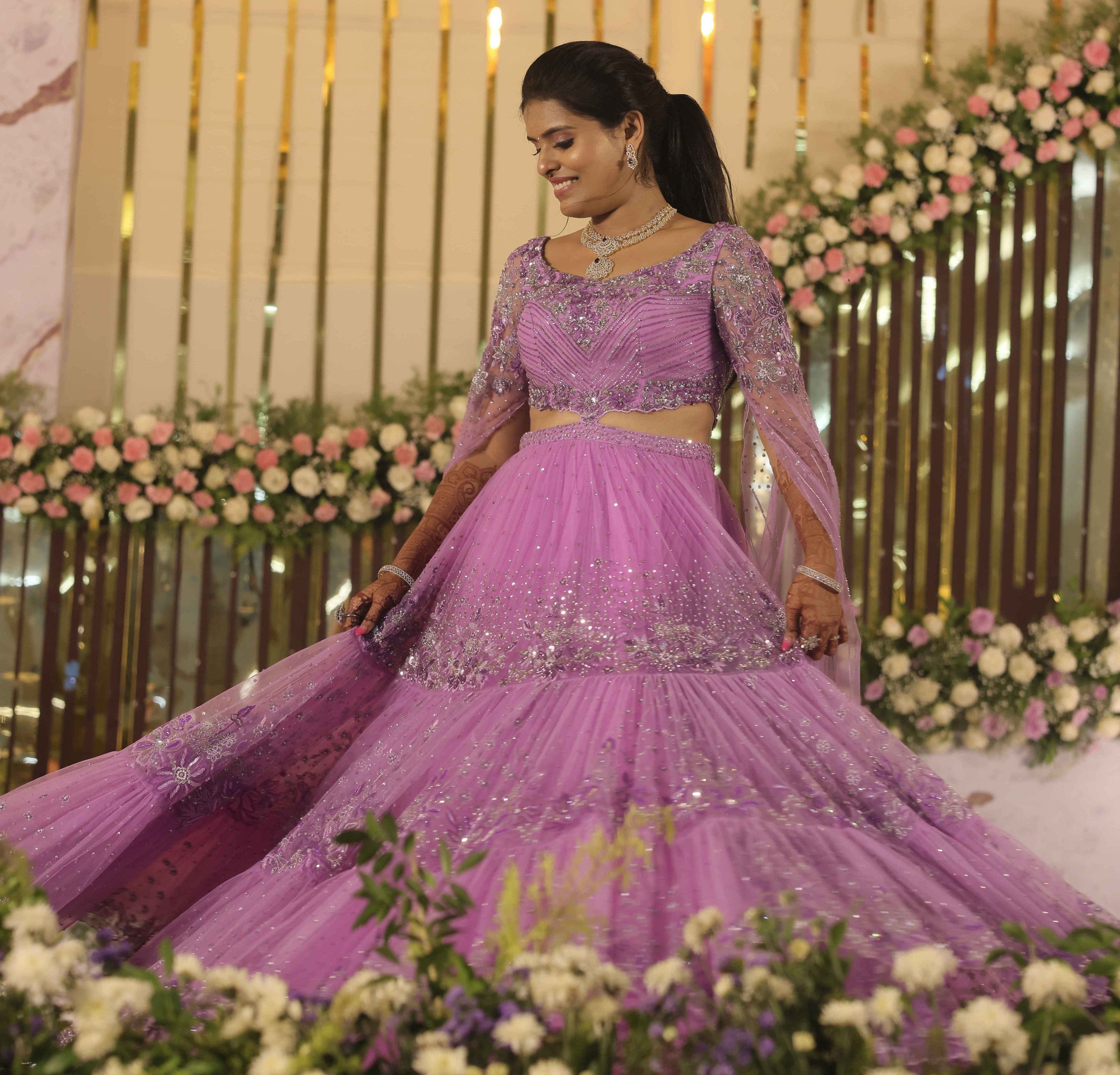 Bride in a lavender handcrafted lehenga with trail sleeves twirling on stage for her reception. The outfits for both the bride and groom is designed by Archana Karthick. Front lehenga design captured.
