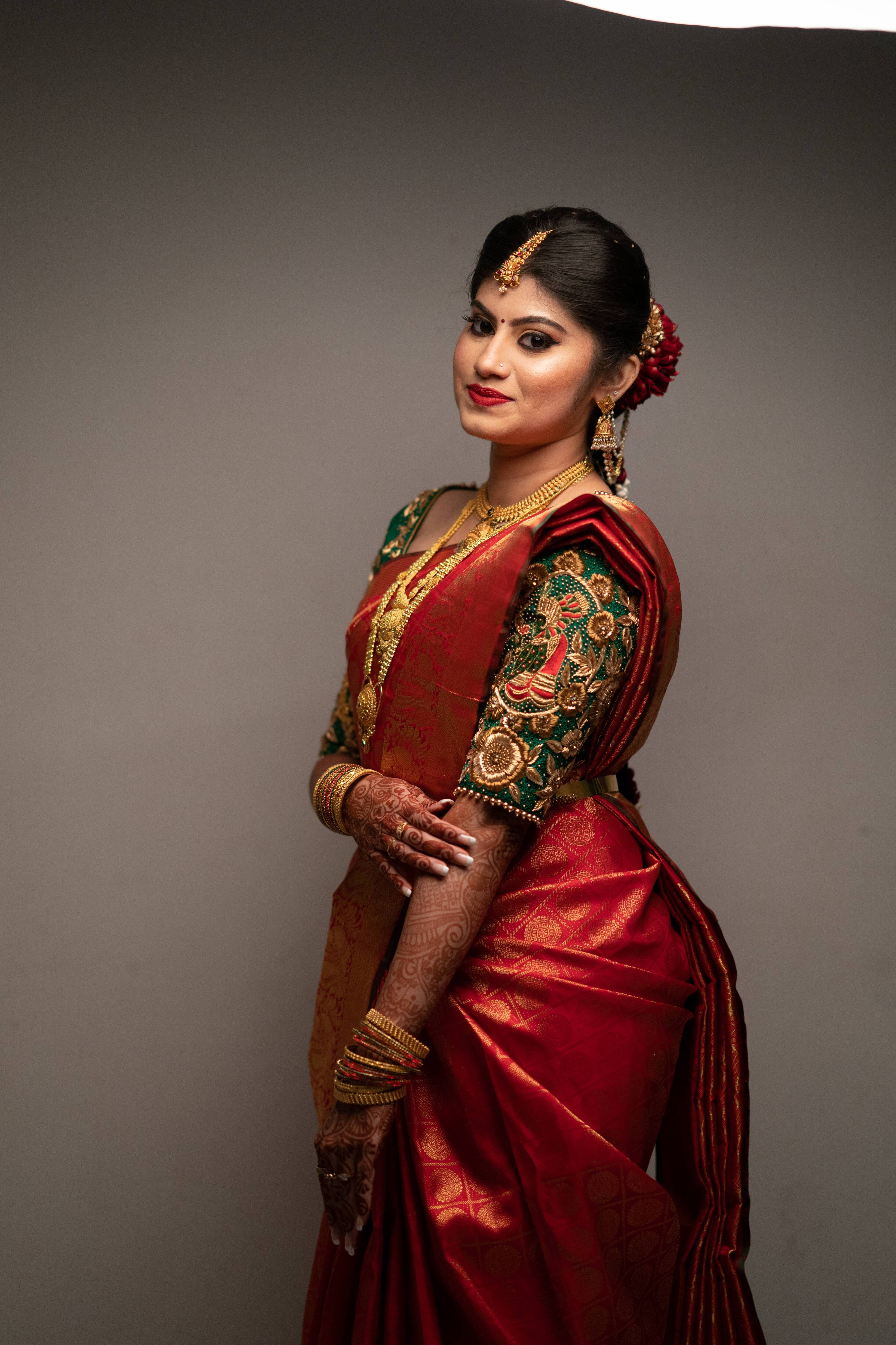 Bride Vandita is seen here in our Handcrafted Concept Bridal Blouse in Bottle Green Raw Silk. She is seen smiling at the camera. Her full side profile is visible clearly showing the intricate embroidery work on her left sleeve .