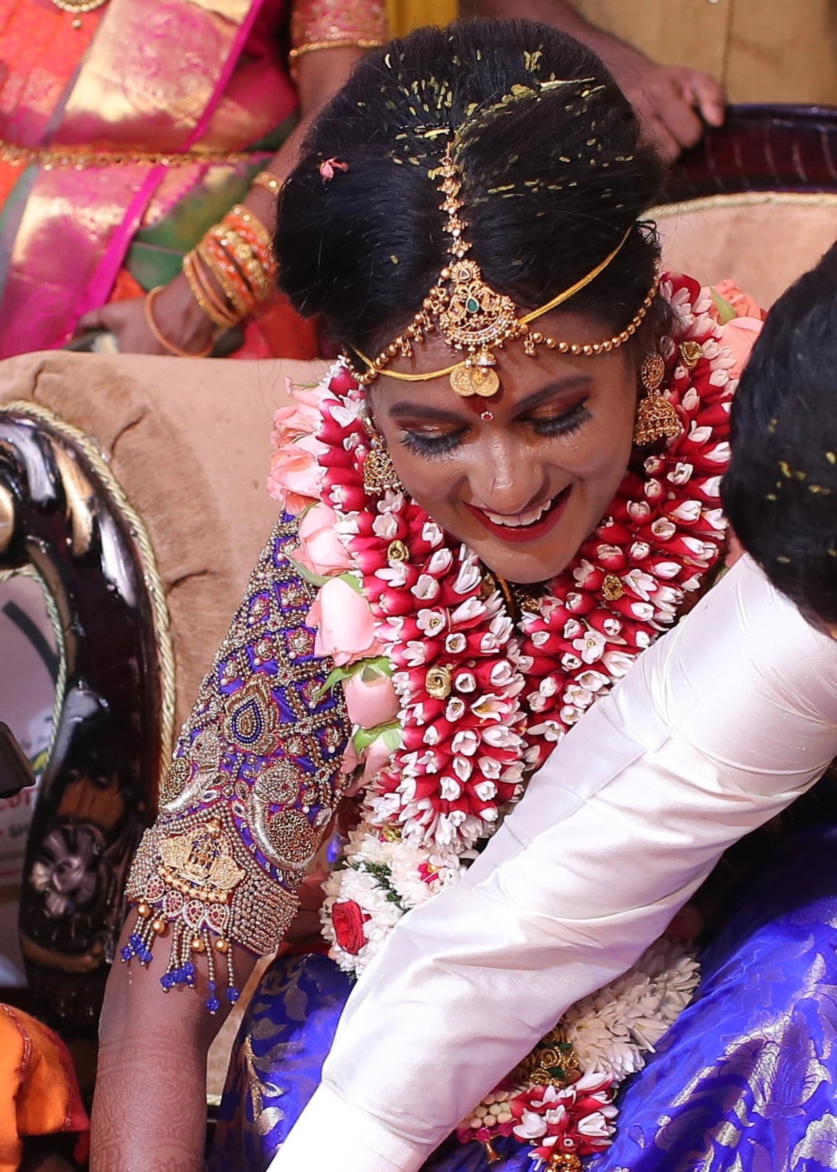 Bride laughing in a concept peacock blouse in blue and red silk, handcrafted with zardozi, beads, resham knot work and goddess pendant on sleeves.