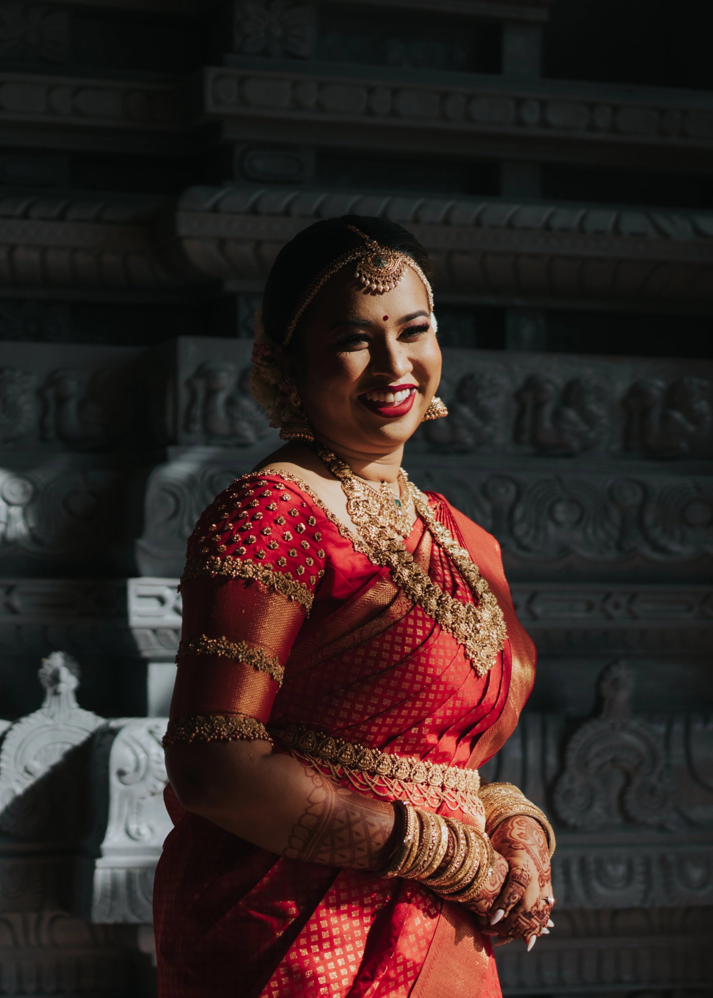 Bride laughing in a handcrafted palanquin concept red silk blouse features zardozi and beads. Designed by Archana Karthick.