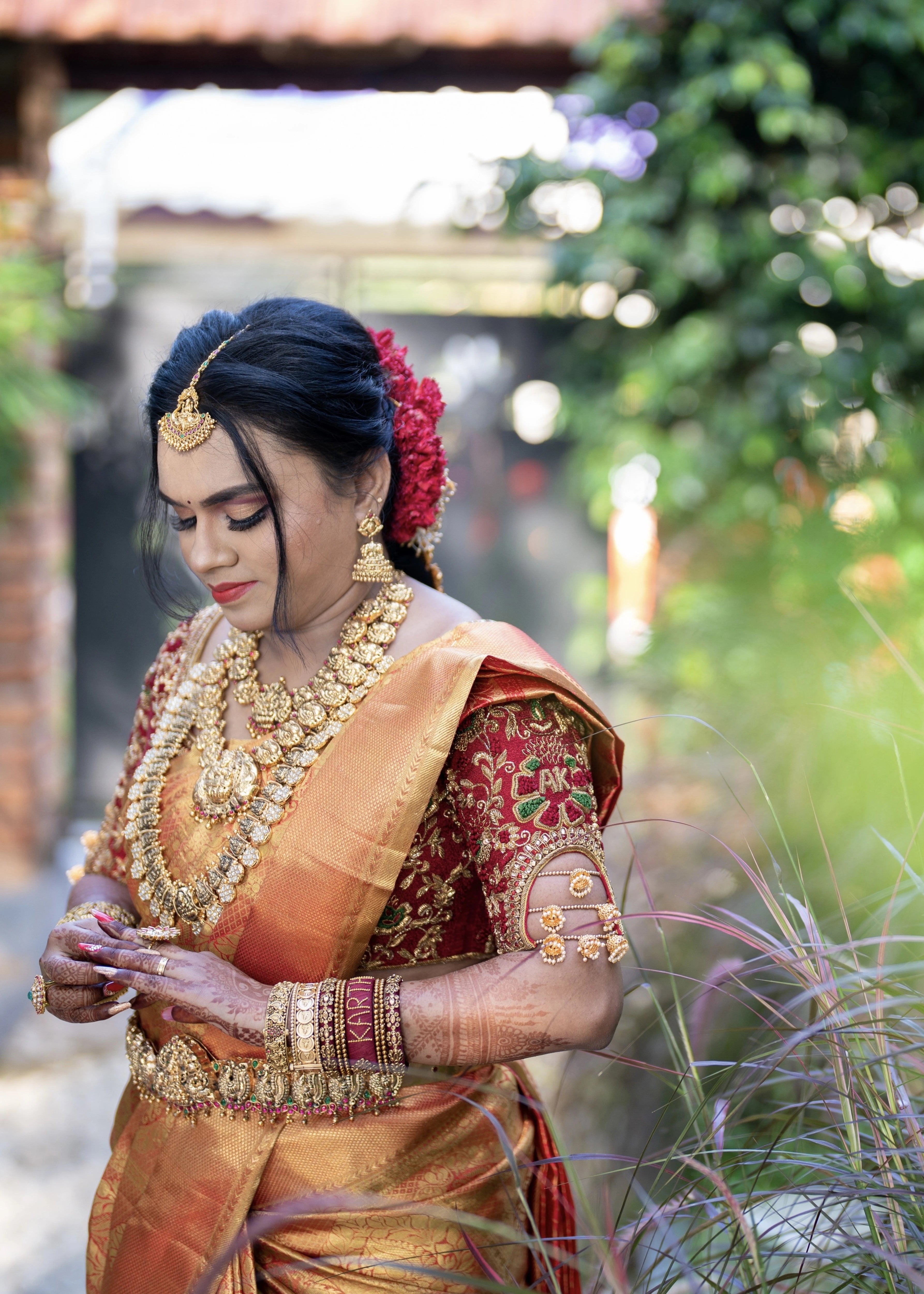 Bride looking down in a red raw silk blouse handcrafted with beads, stones, zardozi, resham knot work and jhumki hangings with creeper motifs designed by Archana Karthick
