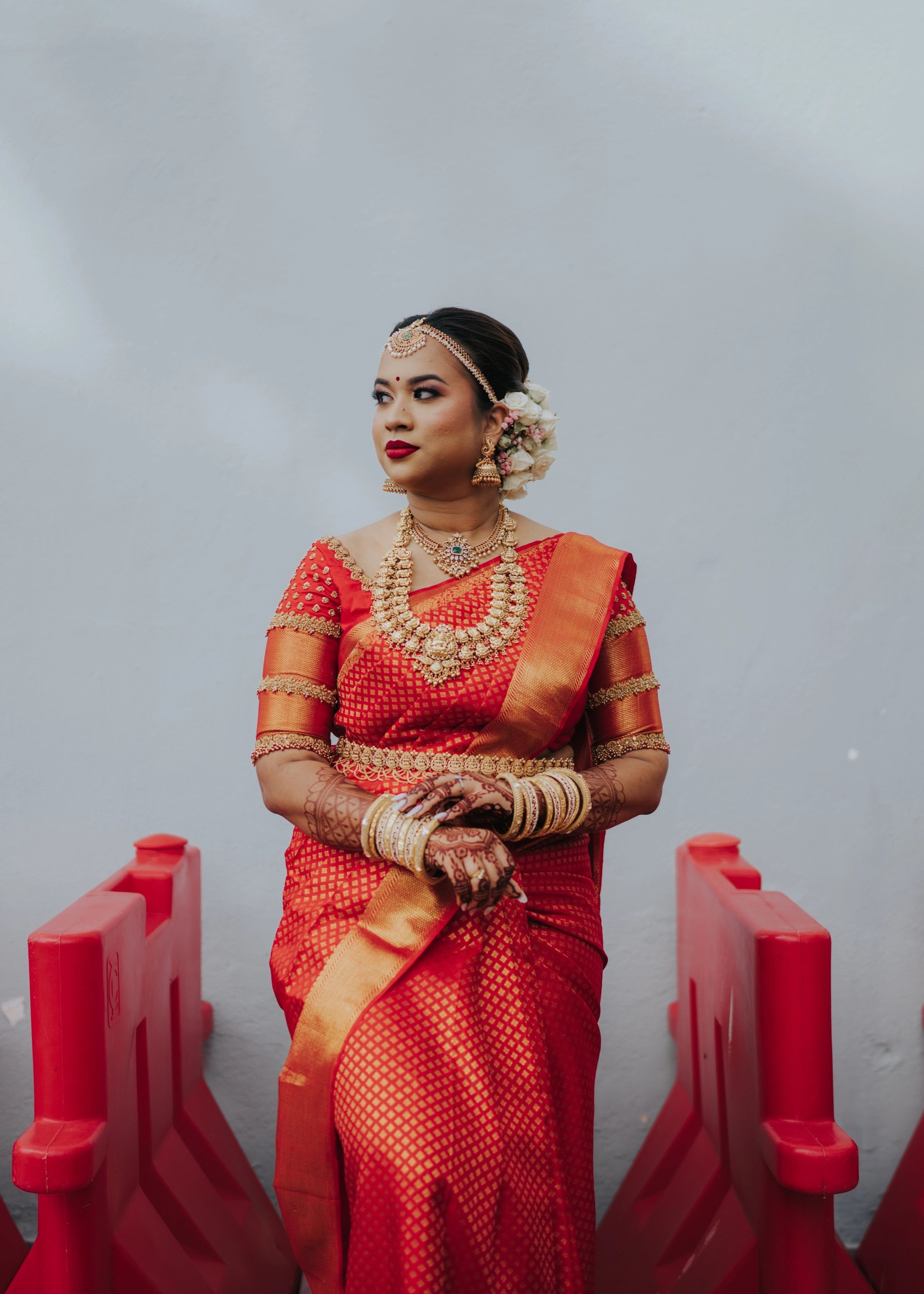 Bride looking right in a handcrafted palanquin concept red silk blouse features zardozi and beads. Designed by Archana Karthick.